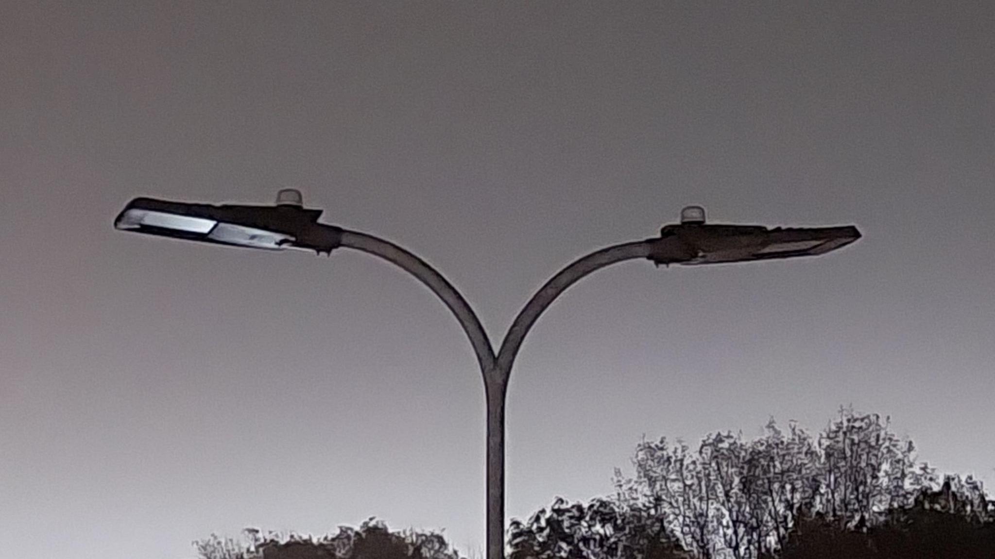 Two streetlights above a road which are not on at night. Trees can be seen in the background.