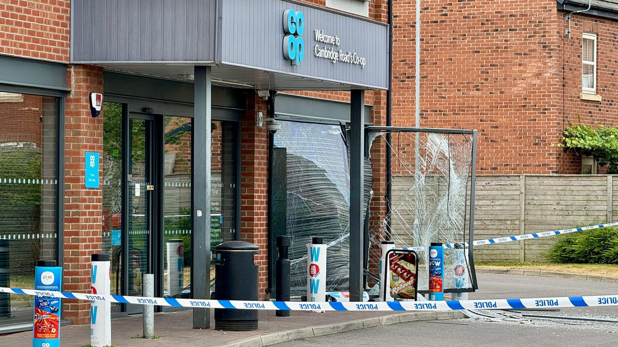 A Co-op store in Whetstone, Leicestershire, with police tape around it. A large glass window has been smashed and the frame pulled away from building with a shutter damaged.
