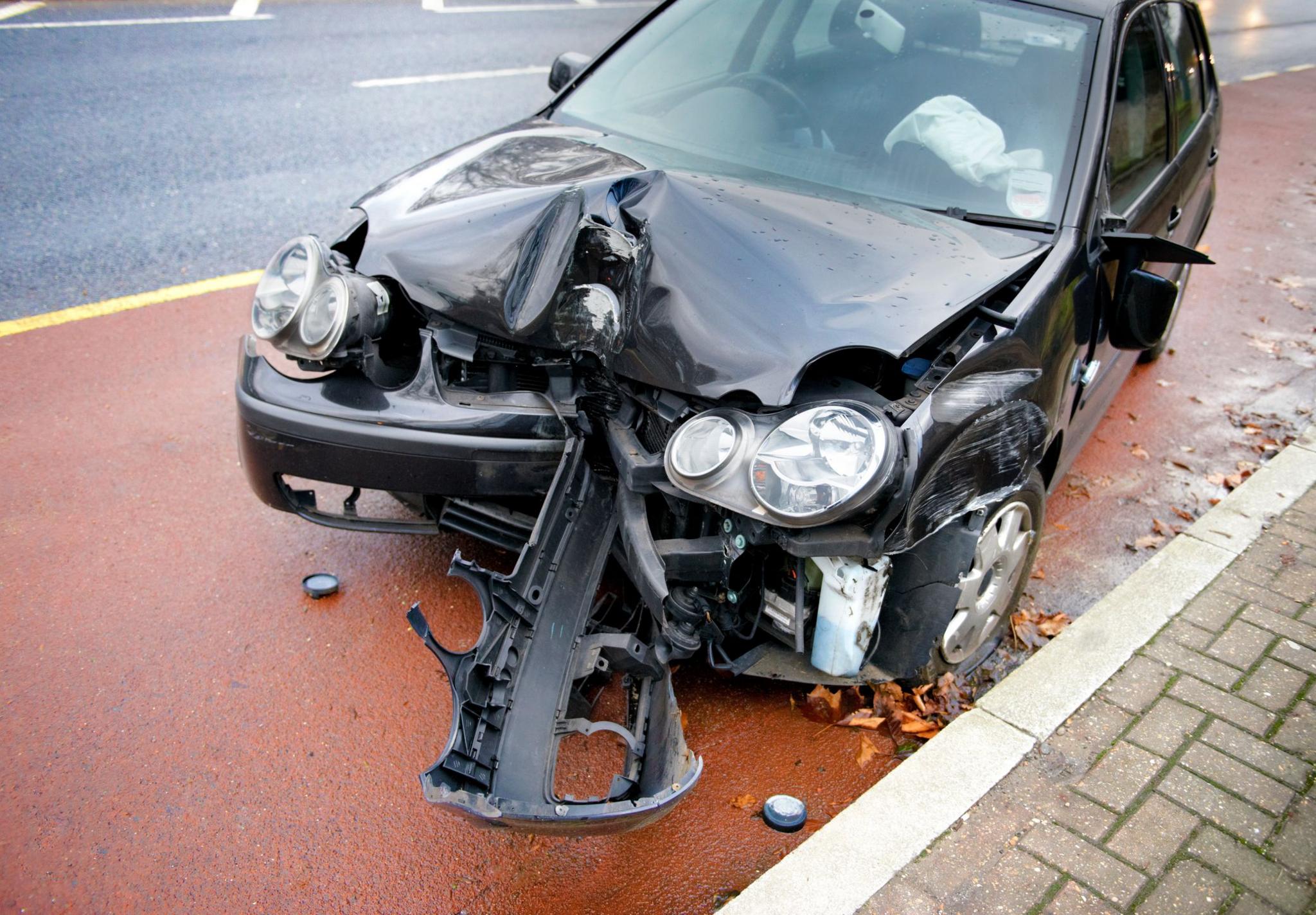 A black car at the side of the road following a collision, with its front bonnet crushed