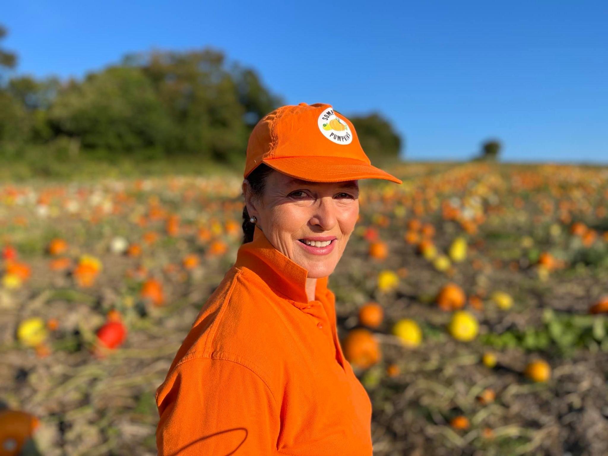 Farmer Caroline Harriott wearing orange and standing in a field with hundreds of pumpkins behind her.