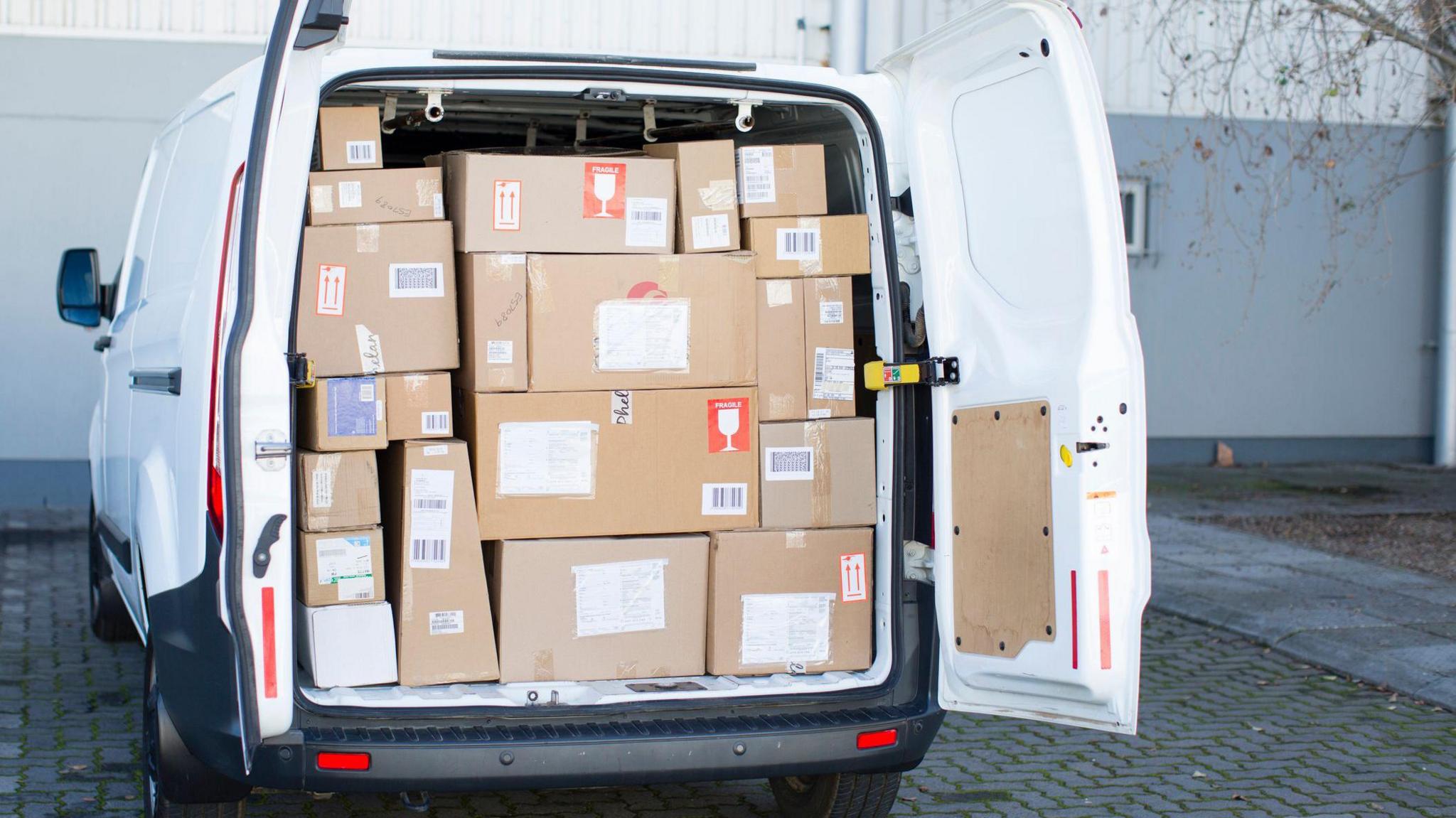 A white delivery van with the back doors open showing it to be full of parcels.