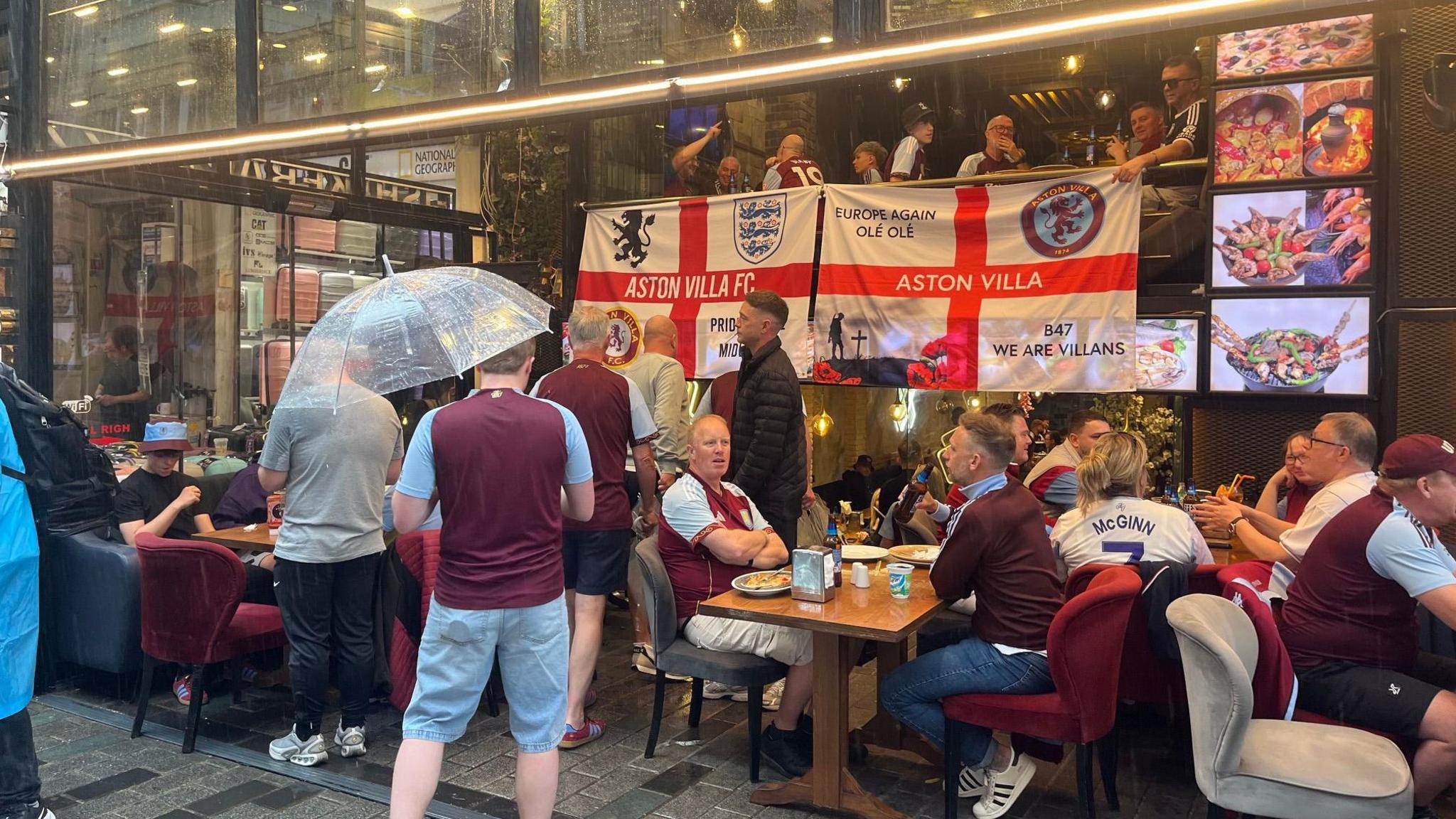 Aston Villa fans in Istanbul drink in a bar, while umbrellas can be seen being held by some
