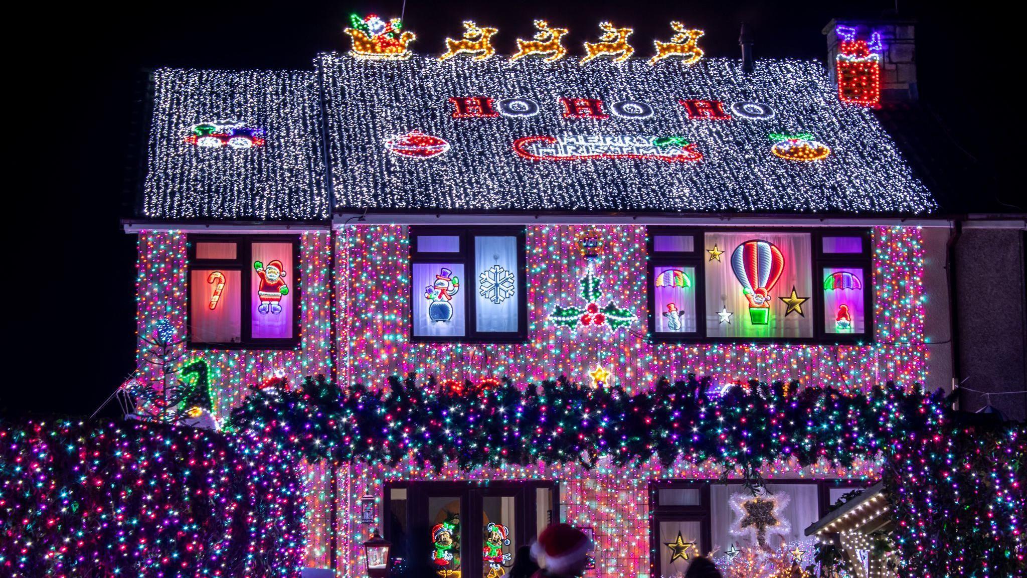 A house covered in Bright blue and purple Christmas lights on a house in Winterbourne near Bristol. On the roof of the house, lights spell out Ho Ho Ho.