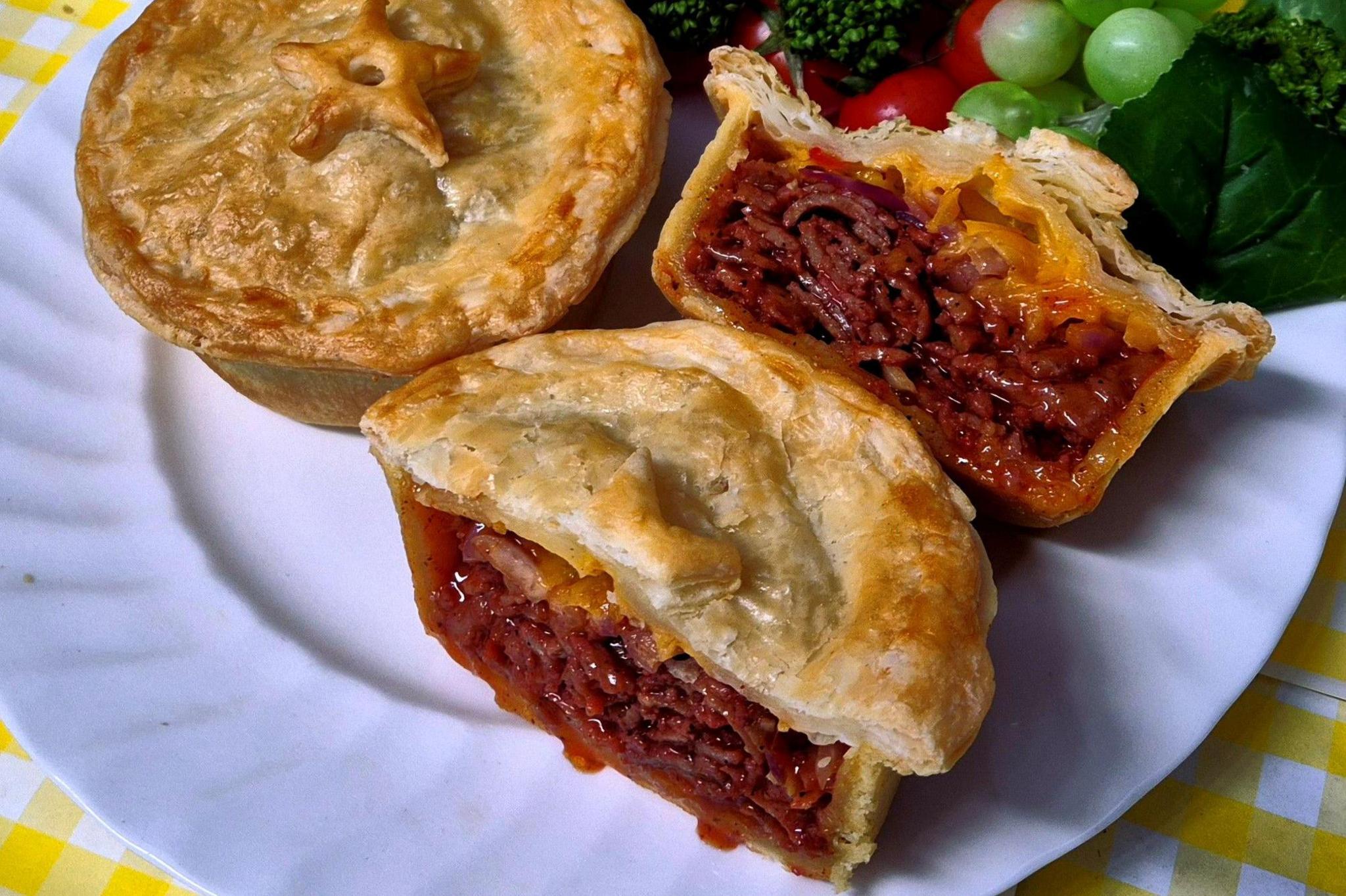 Two pies are on a plate. One is cut open to reveal a dark brown kebab meat.