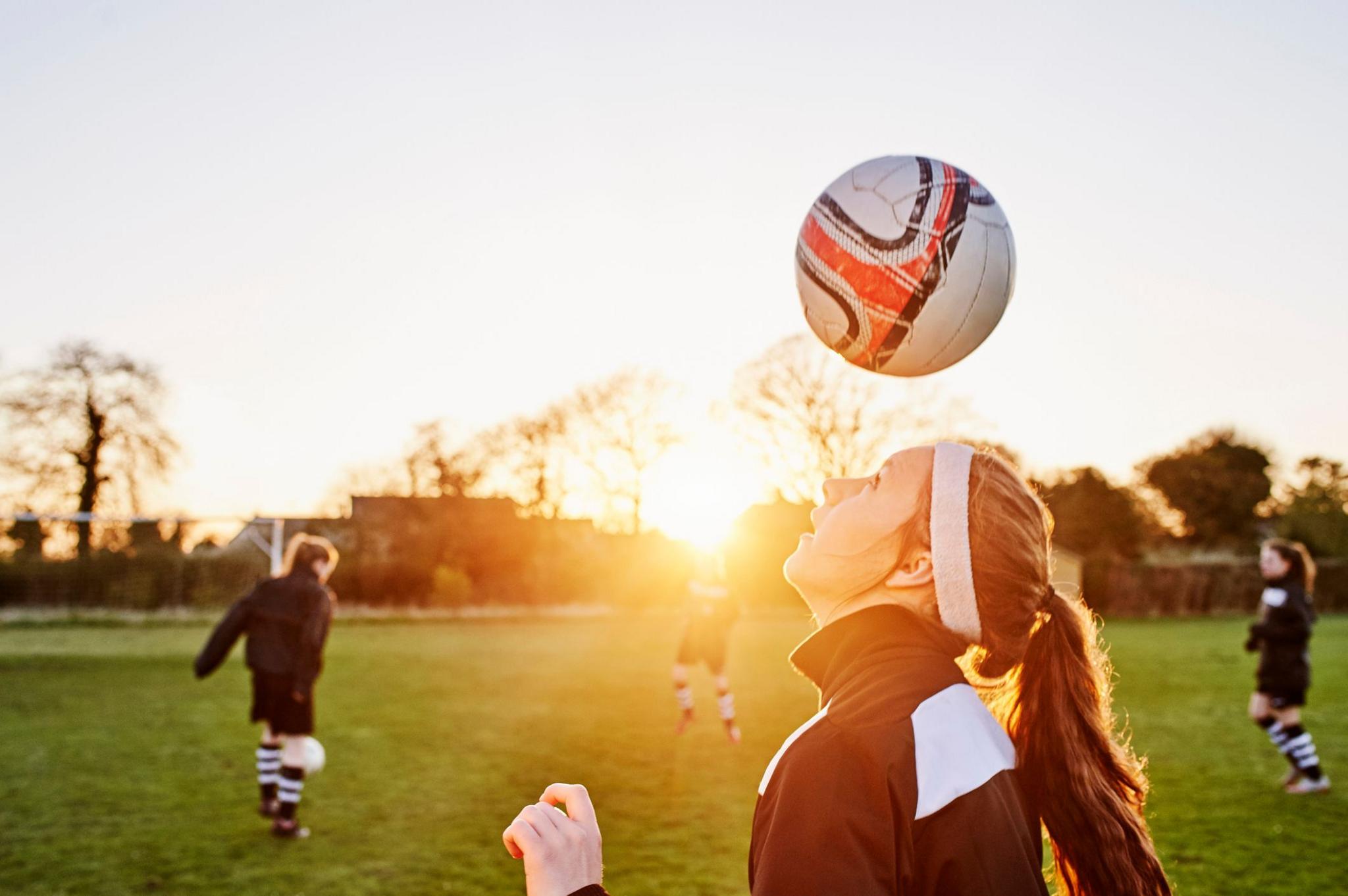 A girl with a headband and ponytail heads the ball. 