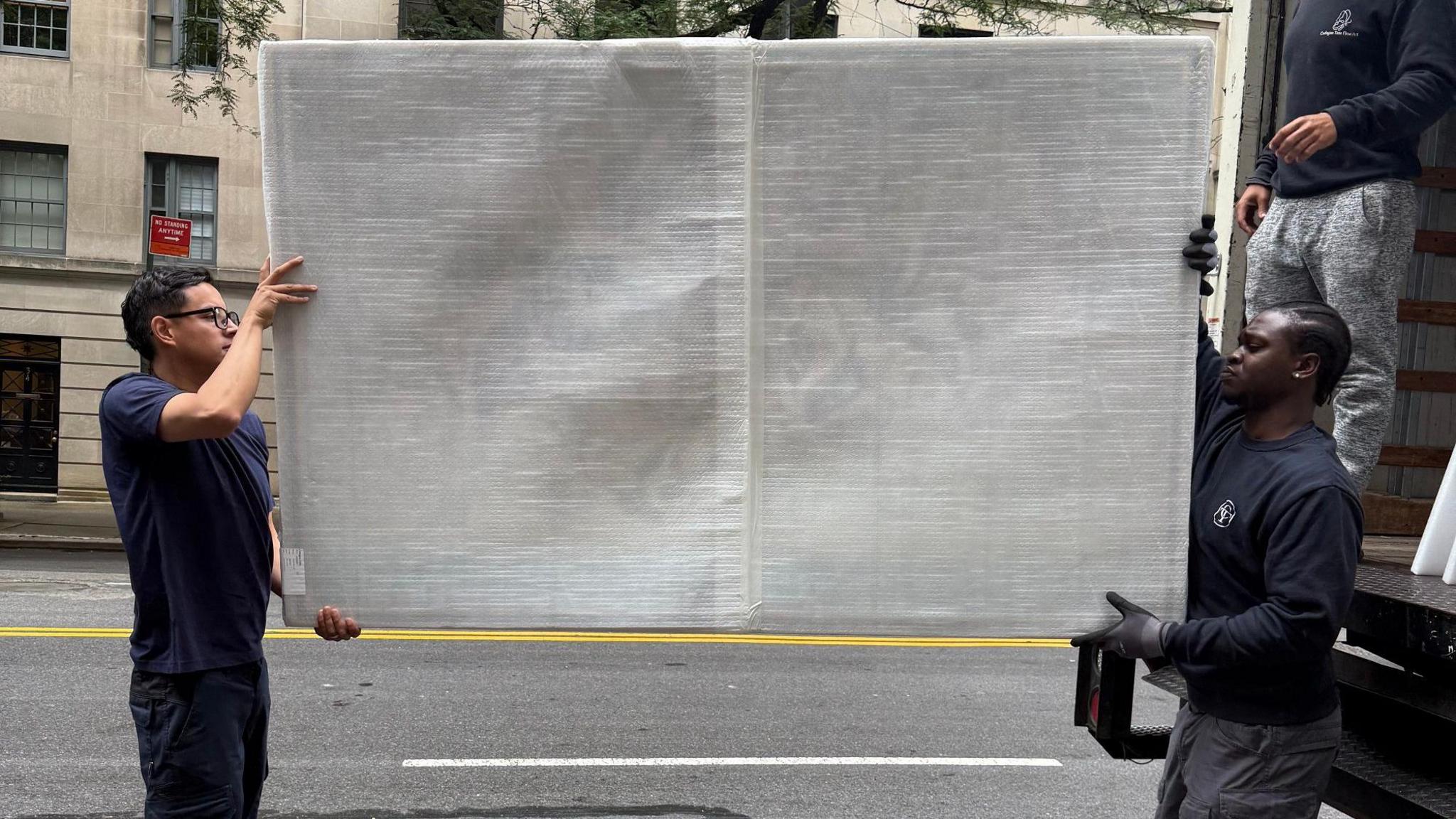 People unload a large wrapped Henry Orlik canvas from the back of a lorry in New York
