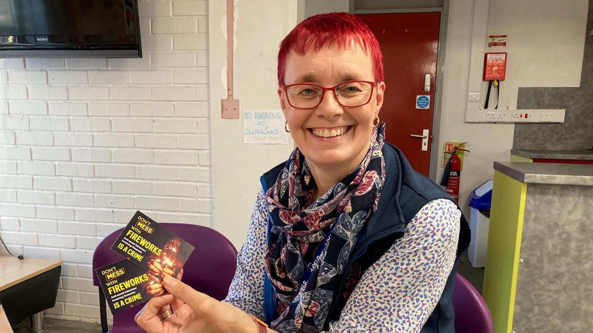 A woman with dyed red hair holds two of the Consequences Cards in her left hand.