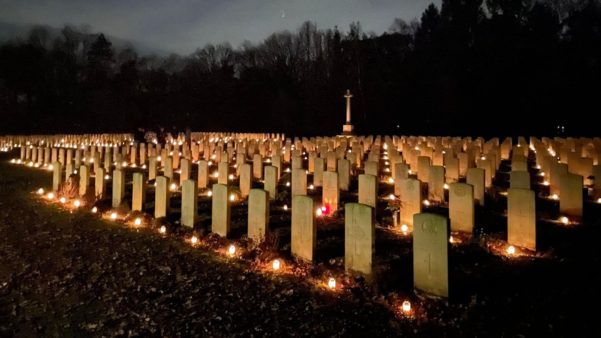 Stone graves in a war cemetery are lit up at night by candles 