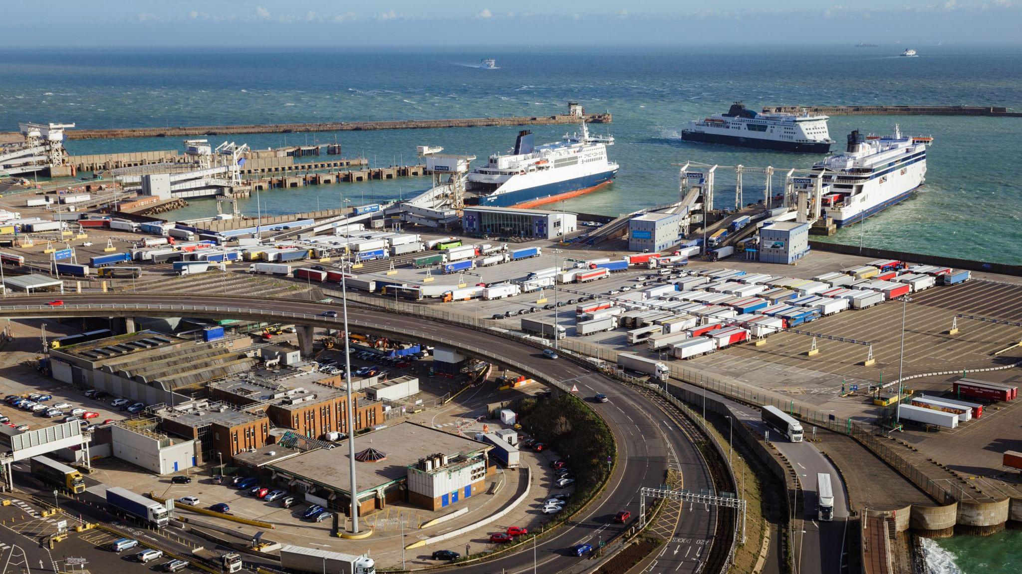 A large industrial port with big boats being loaded with lorries and cars.