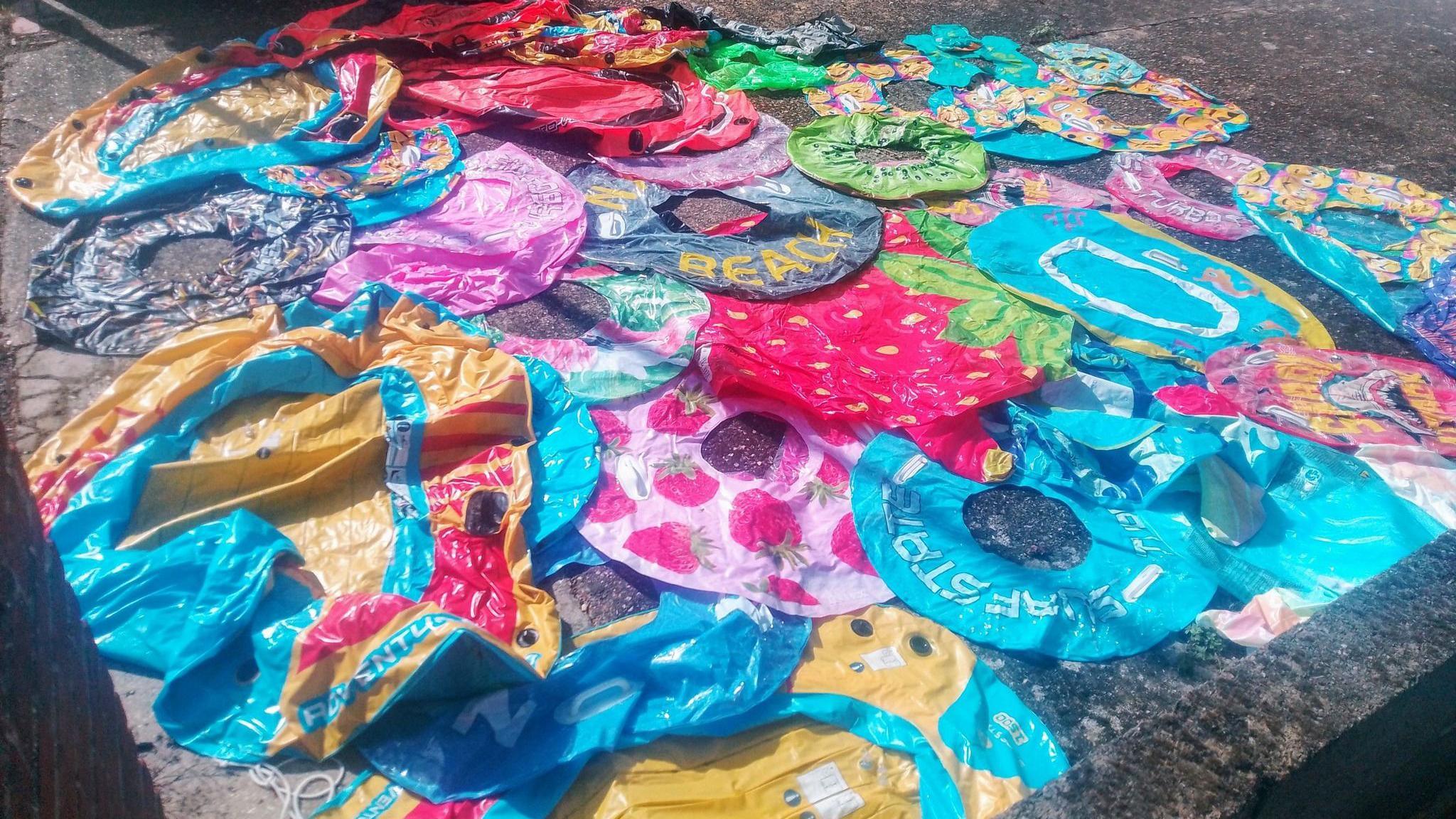 Large number of deflated beach inflatables spread out on concrete.
