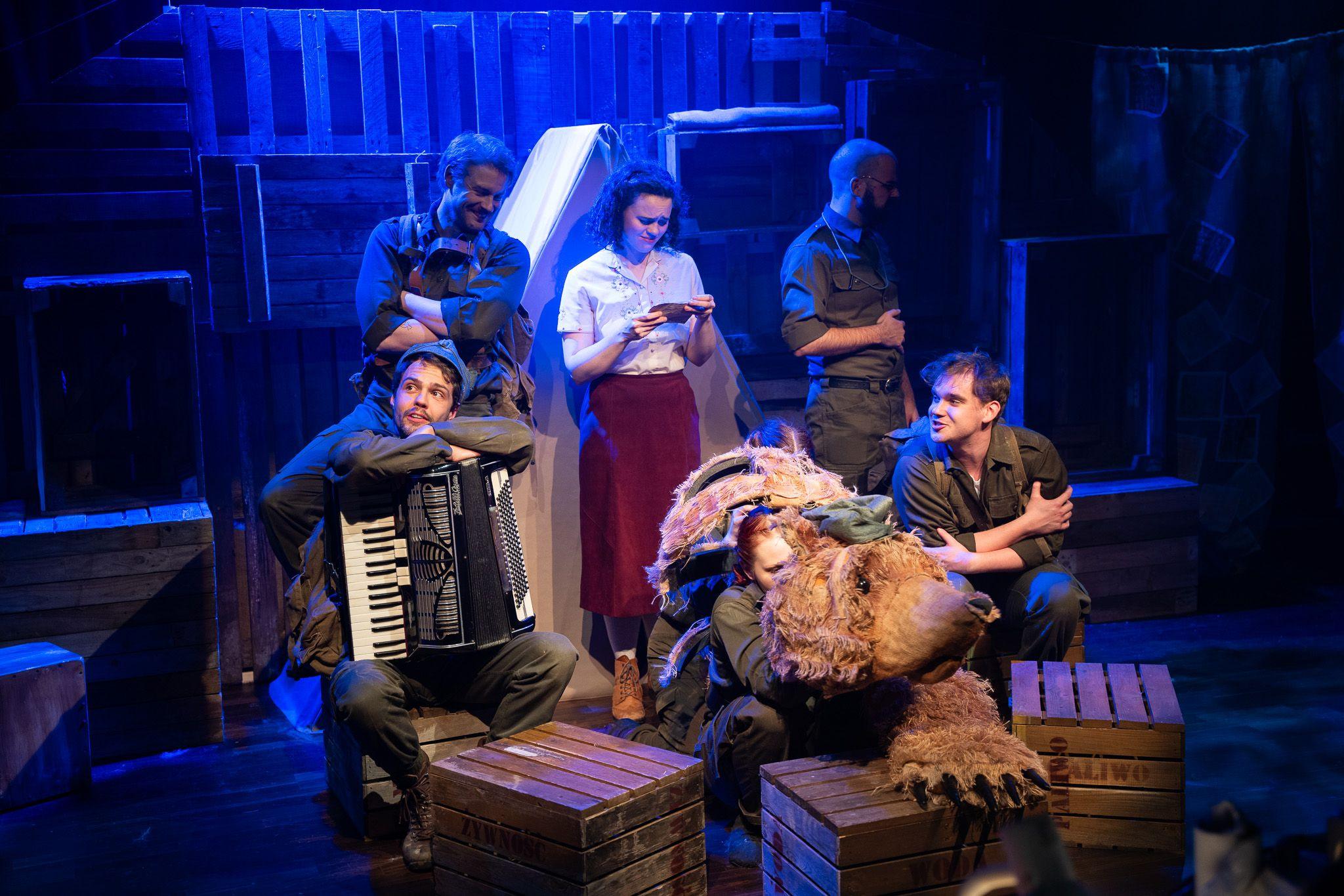 Actors rehearse for a production of The Bear Who Went to War. They can be seen holding an accordian with an actor dressed as Wojetek the bear