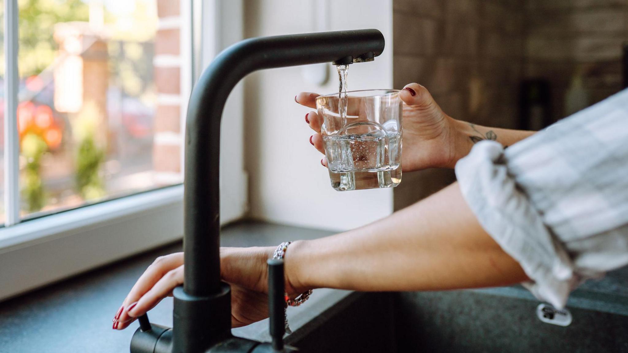 A person filling a glass with water from a tap