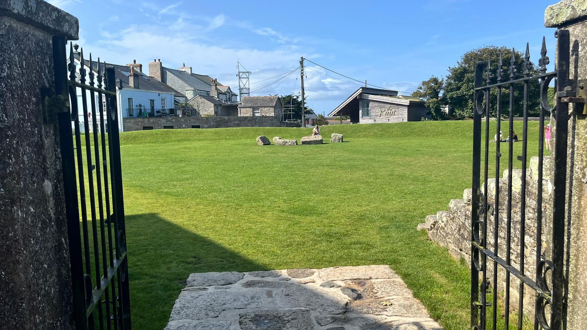 The Plen an Gwari in St Just, an open grassy ampitheatre with banked sides, viewed through a granite gateway and open black metal gates.