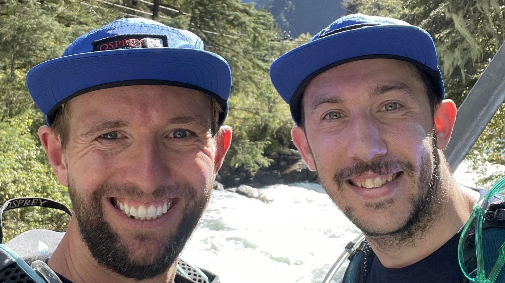 The faces of two bearded men wearing blue peaked caps smiling. The word "OSPREY" can be seen on the cap of the man on the left.