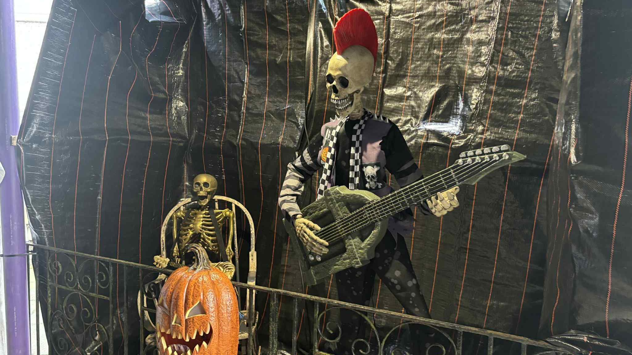 A skeleton model on display, with a fake guitar and a red mohawk. Another smaller skeleton is next to it, and a pumpkin with a carved face sits in front of them.
