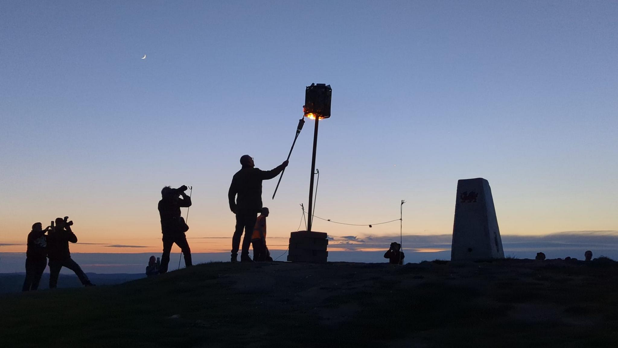 Silhouettes of people lighting a beacon on the Garth