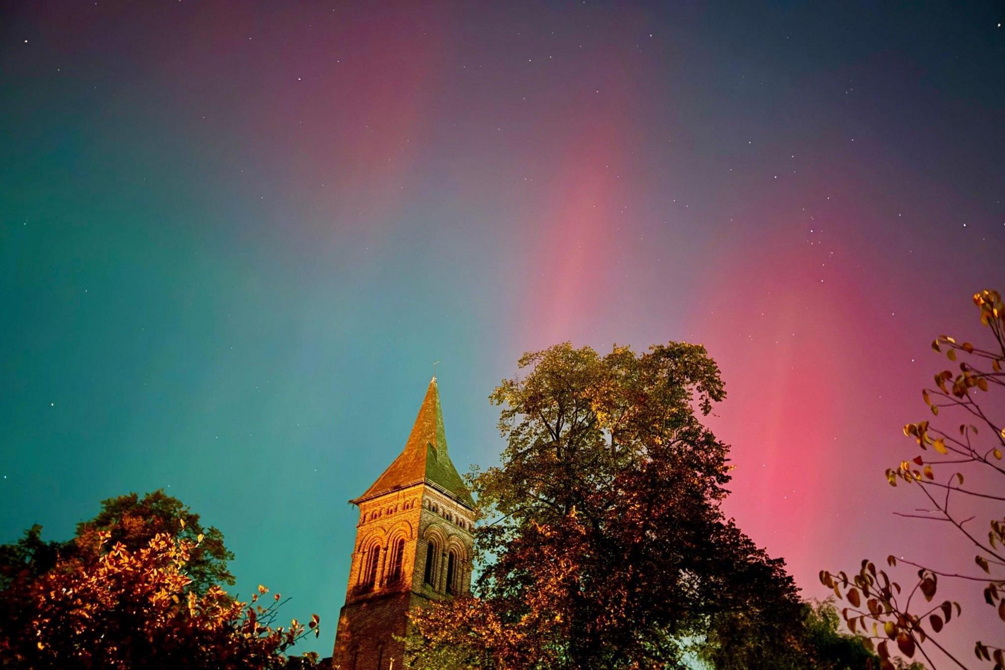 Pink and blue Northern Lights over a church steeple and a tree