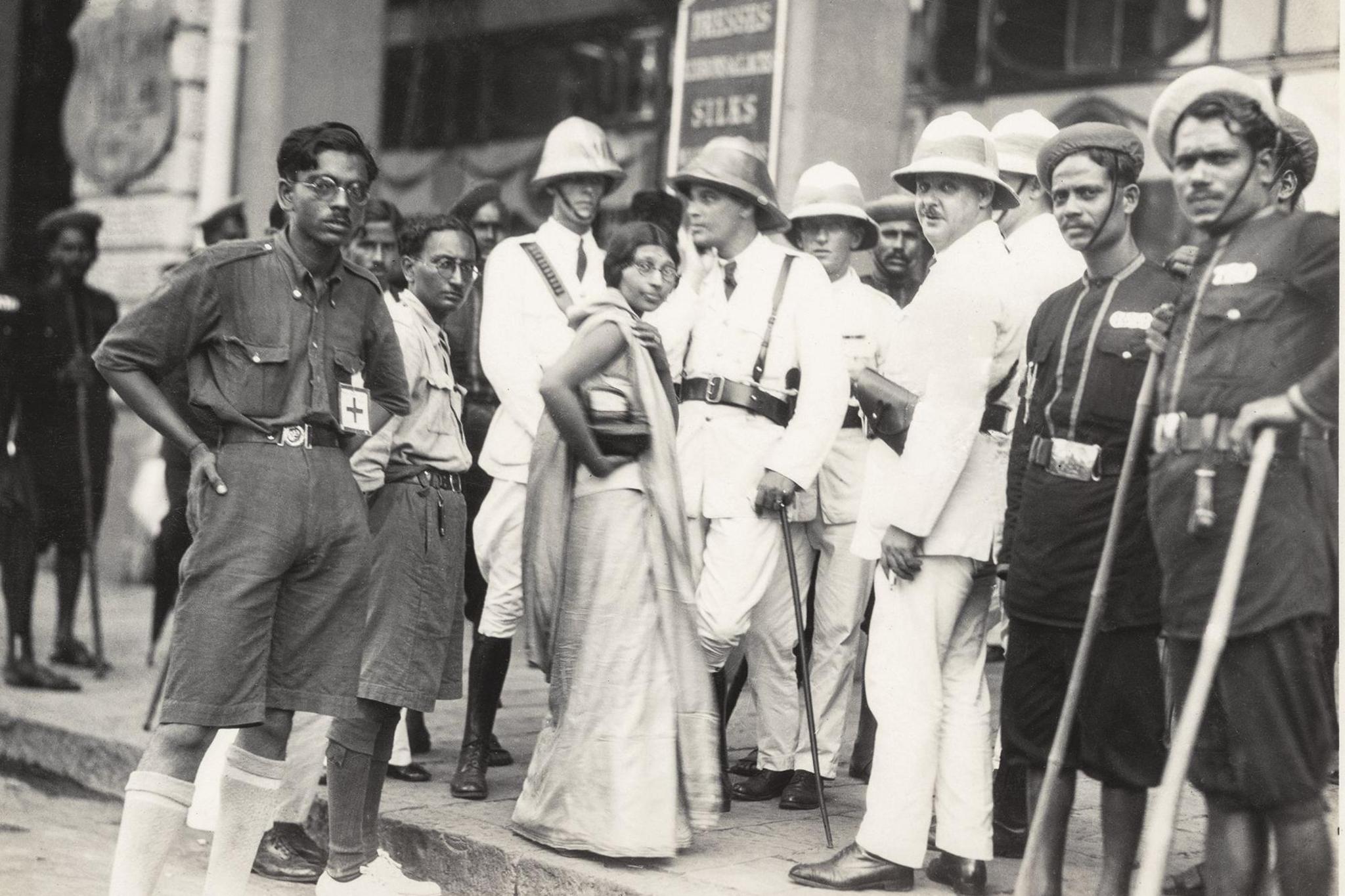 In this monochrome photo, Lilavati Munshi, a Congress leader from Gujarat, stands defiantly outside a boycotted British store in Mumbai. She is wearing a sari and glasses, and is surrounded by the police