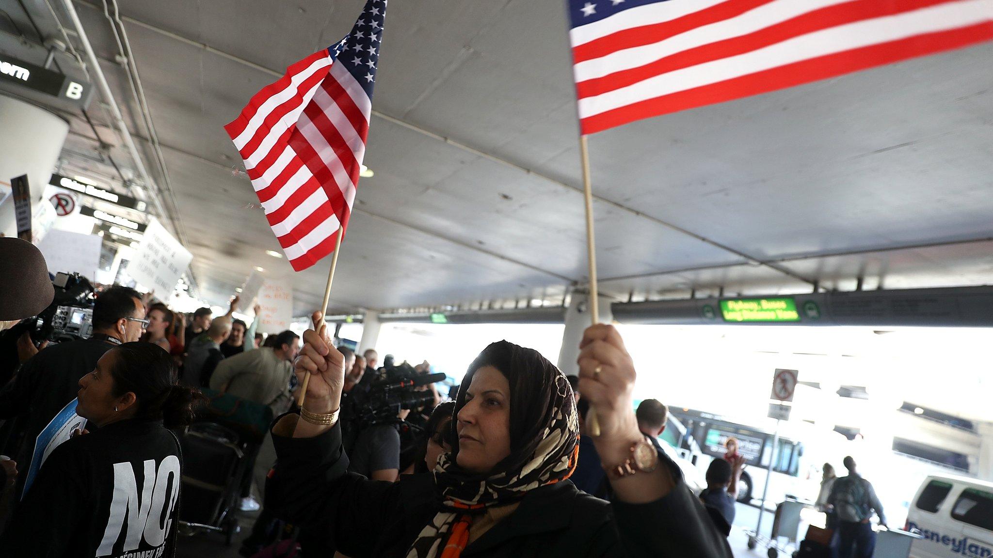 A protester waves American flags during a demonstration against the immigration ban that was imposed by U.S. President Donald Trump at Los Angeles International Airport on January 29,