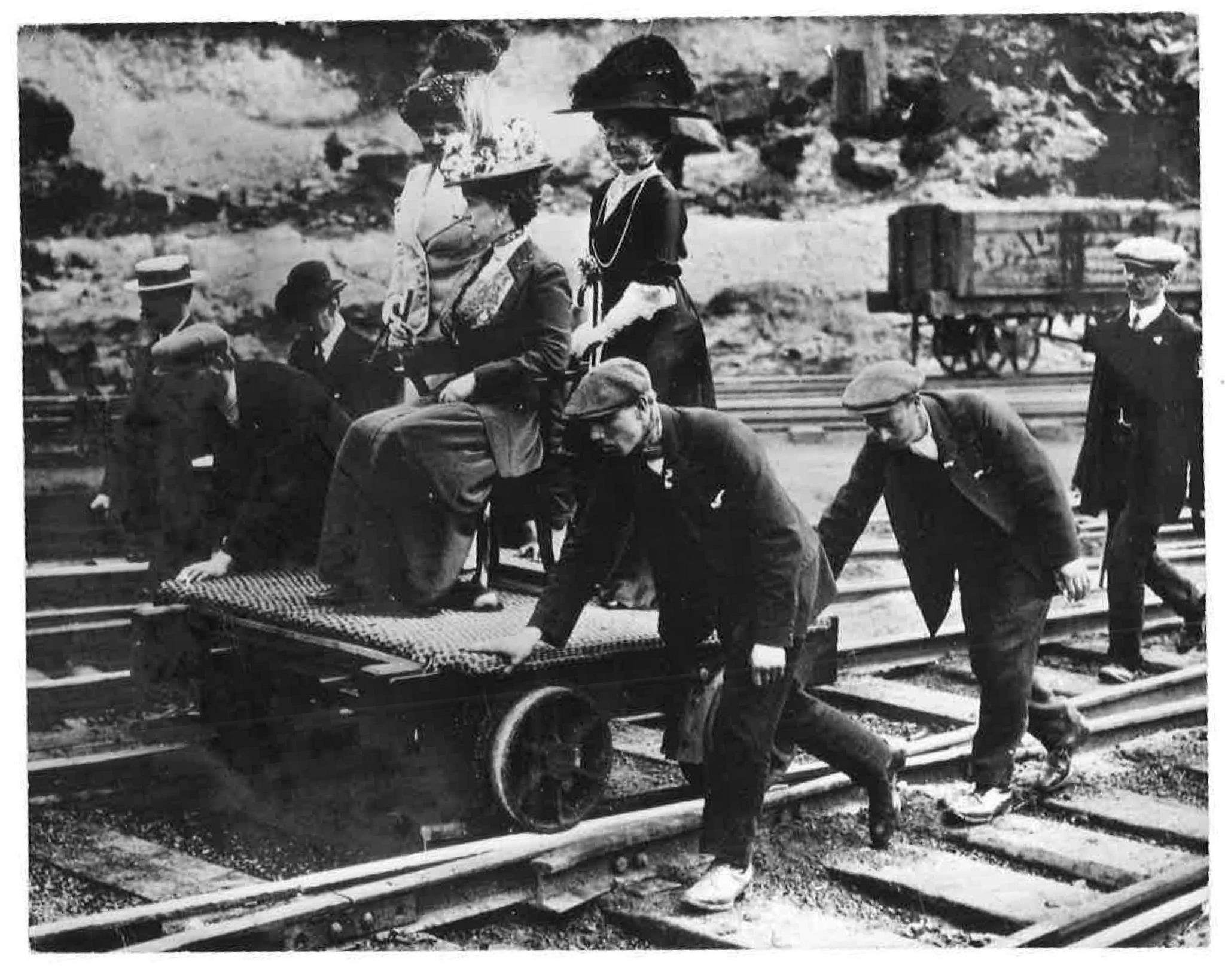 A black and white image of a woman sitting on a chair being pushed along a railway track