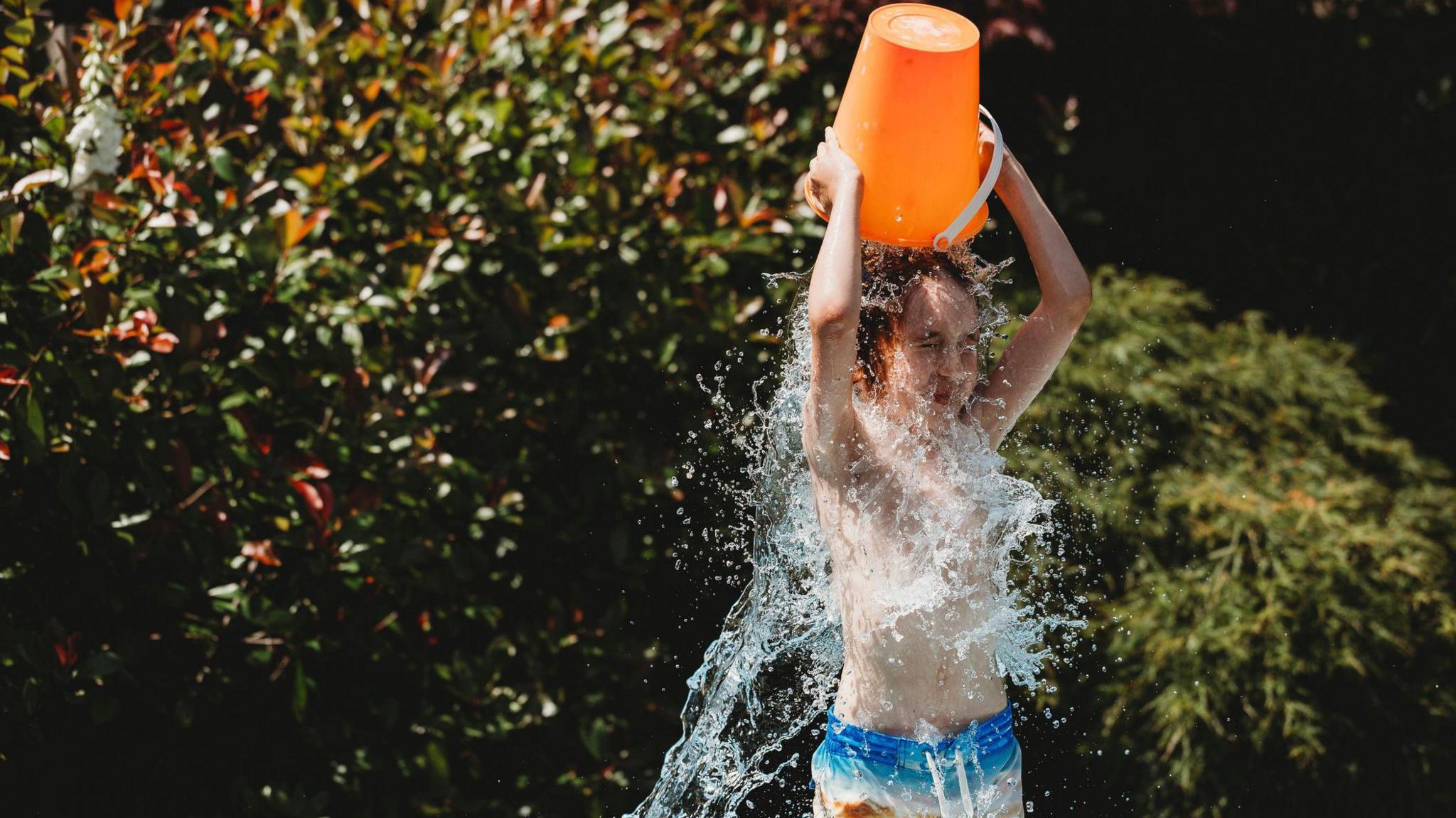 A child chucks a bucket of cold water on his head. 