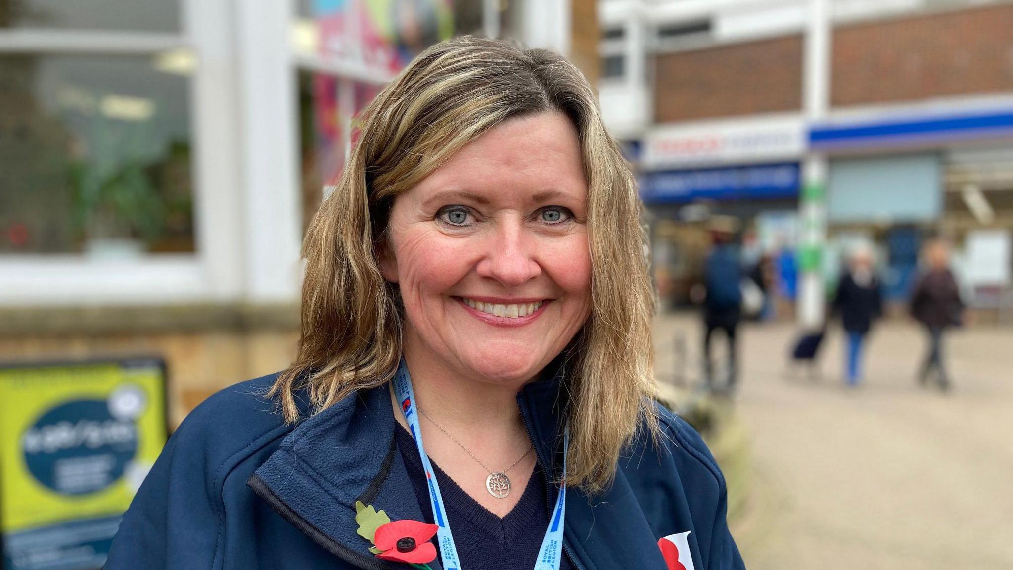 A woman wearing two poppies and a poppy lanyard stood smiling in a town centre