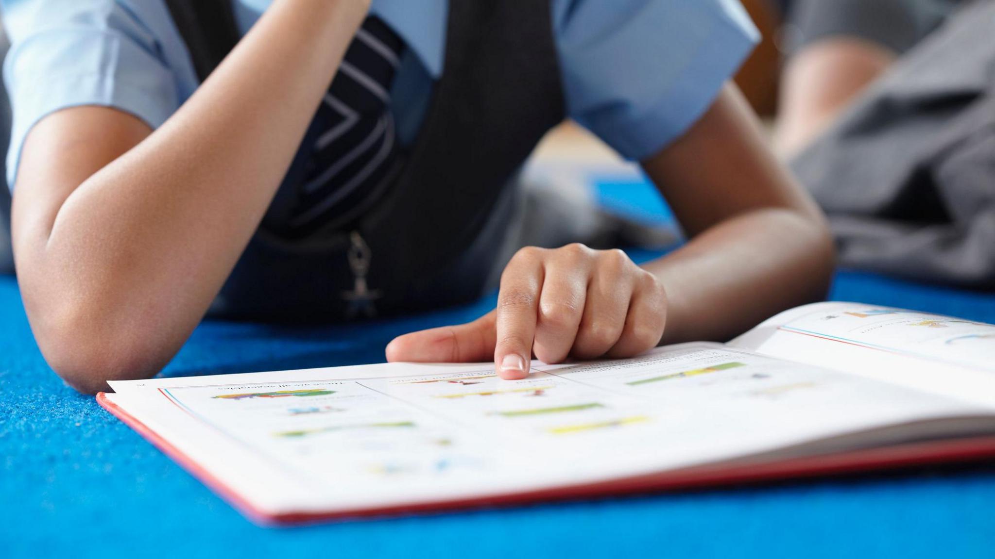 A stock image of a female student reading a book. She is using her finger to trace words. 