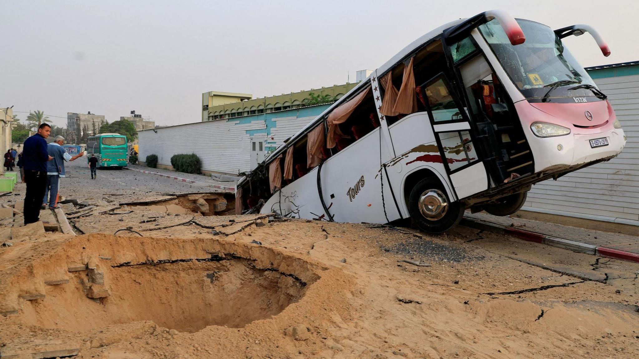 Palestinians inspect a coach dangling out of a crater following an Israeli air strike in the European hospital complex in Khan Younis, southern Gaza (13 May 2025)