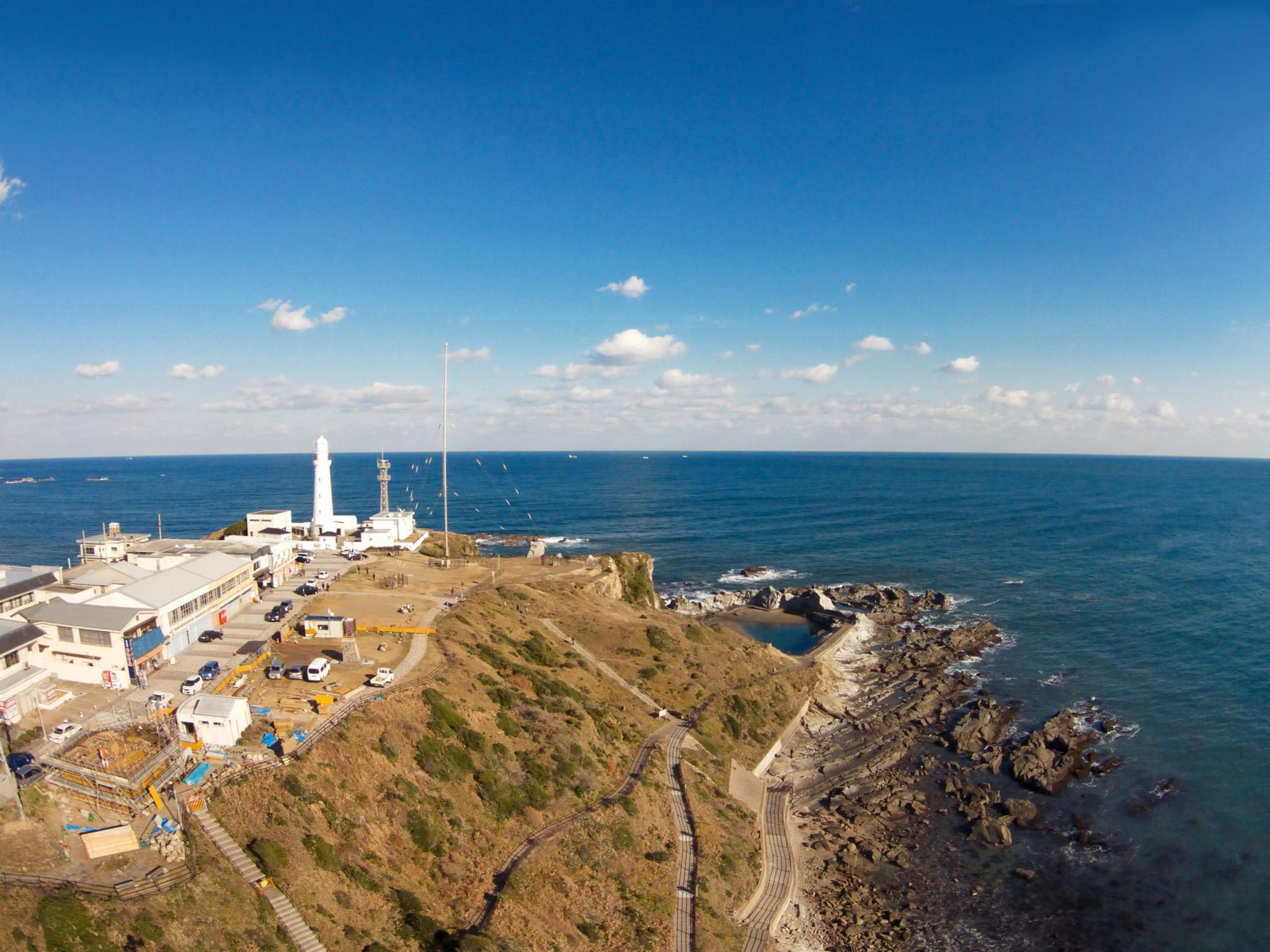 A distant view of an outcrop of land with a lighthouse at the end looking out over a vast expanse of water