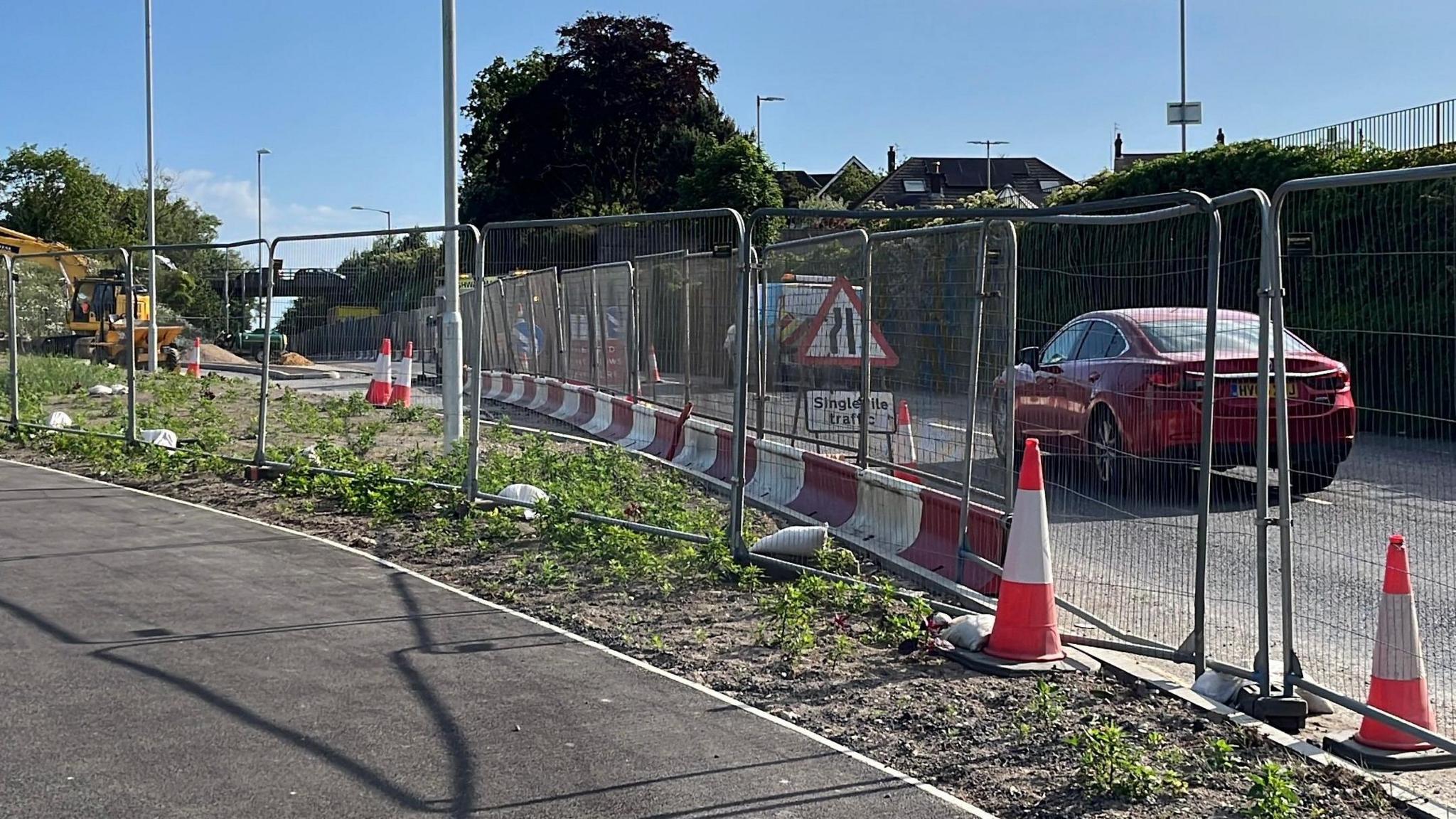 An image of the A21 Sedlescombe Road North which is subject to road works. On the left-hand side a metal railing is visible alongside a red and white cordon.
