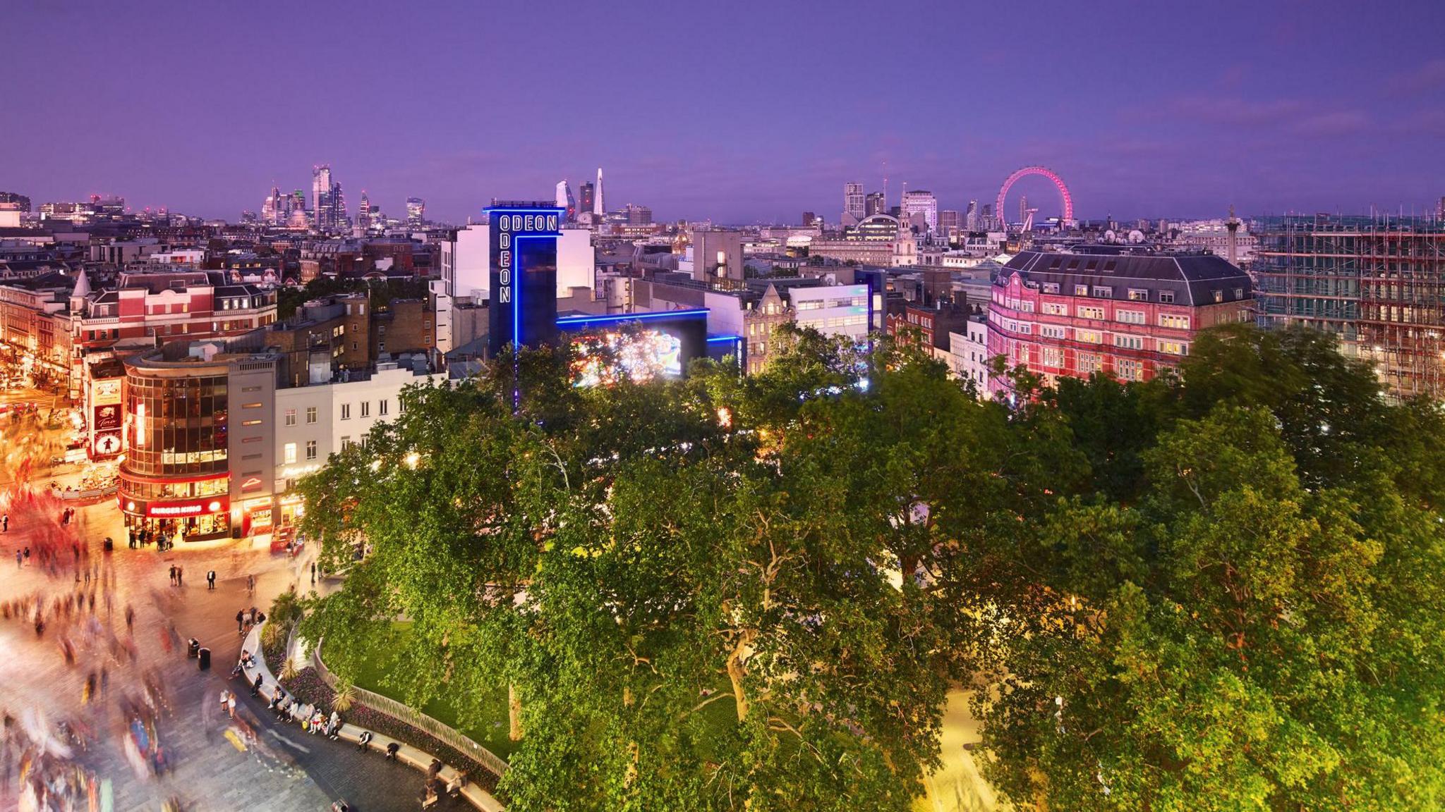 An aerial view of Leicester Square and the surrounding buildings. In the foreground are trees, while in the background the London Eye can be seen as well as the Odeon cinema.