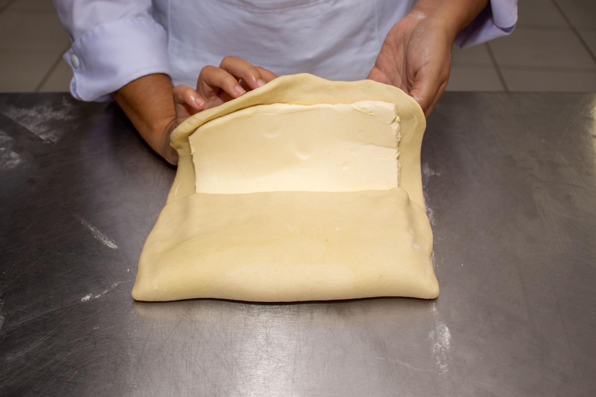 Hands seen opening the dough in a square and applying the butter in three quarters of the dough.