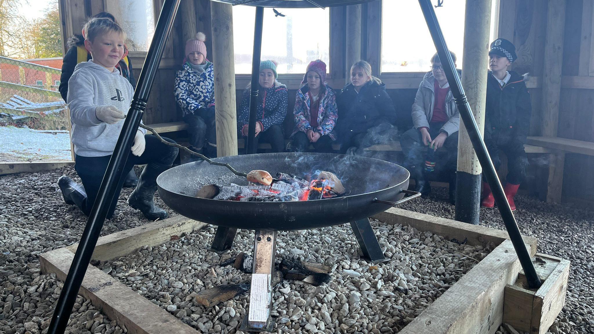 Children toast marshmallows over a fire in their forest school. They are wrapped up in their winter clothes.