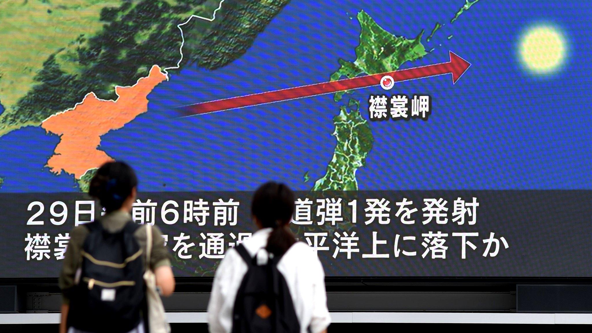 People walking in front of Japanese TV showing missile flight path