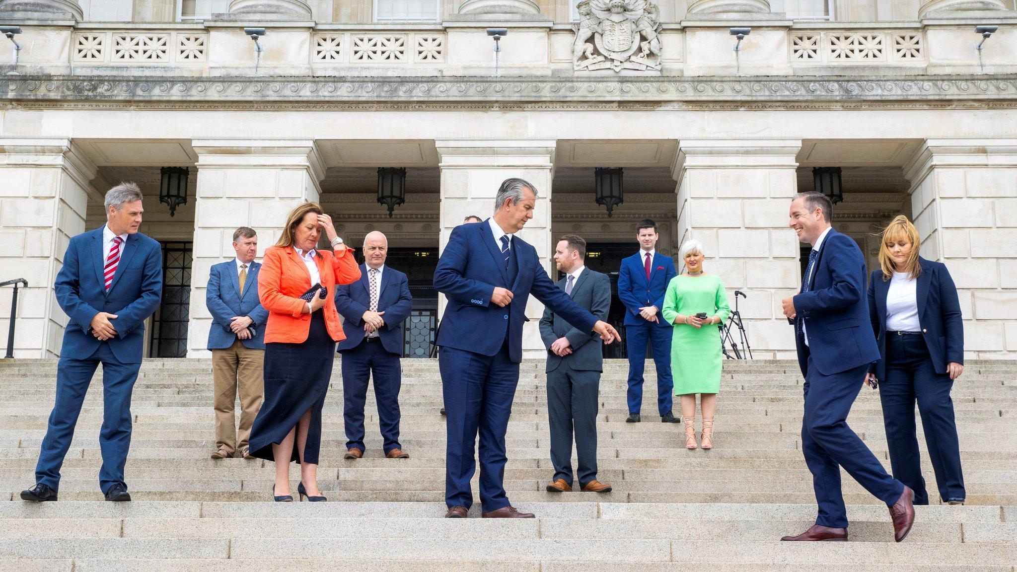 DUP leader Edwin Poots (centre) directs First Minister designate Paul Givan where to stand on the steps on Stormont during a photocall with part of Mr Poots first ministerial team