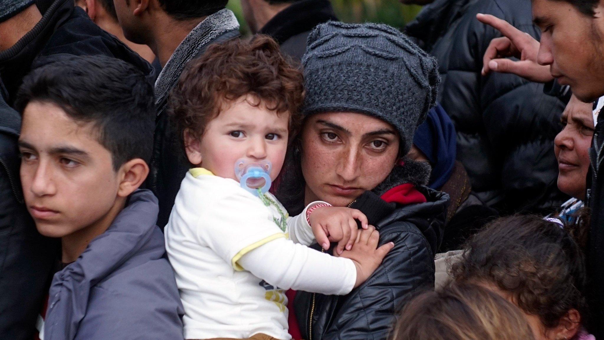 A migrant holds her child in her arms as she waits for their turn at a food distribution stand February 24, 2016