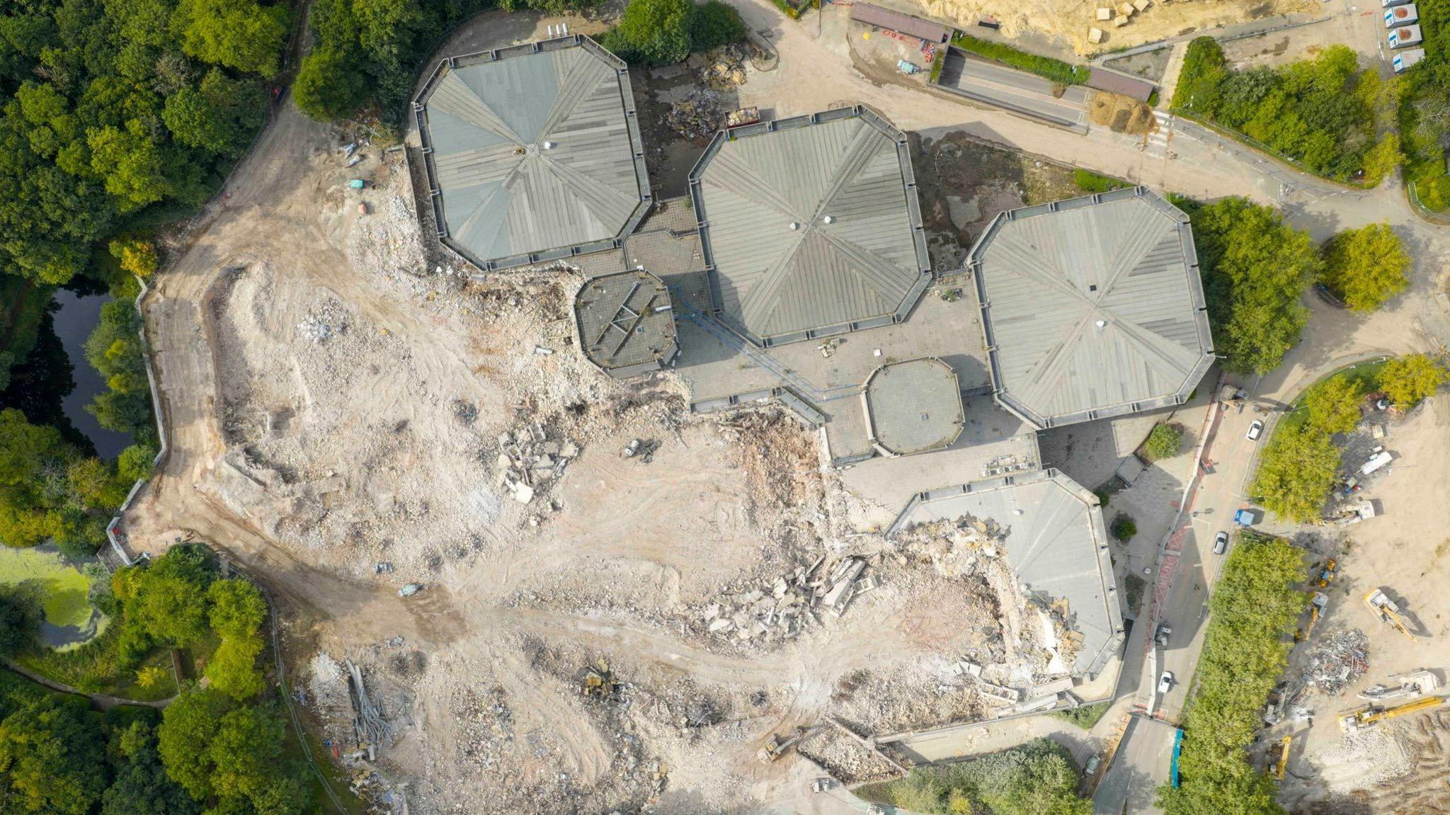 An aerial image of the demolition site, showing three buildings remaining standing and an area of land that is destroyed where the former buildings stood.