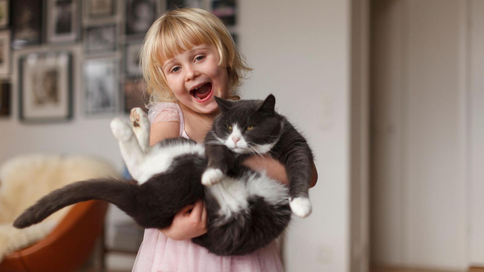 Girl looking very happy holding her cat which looks very grumpy