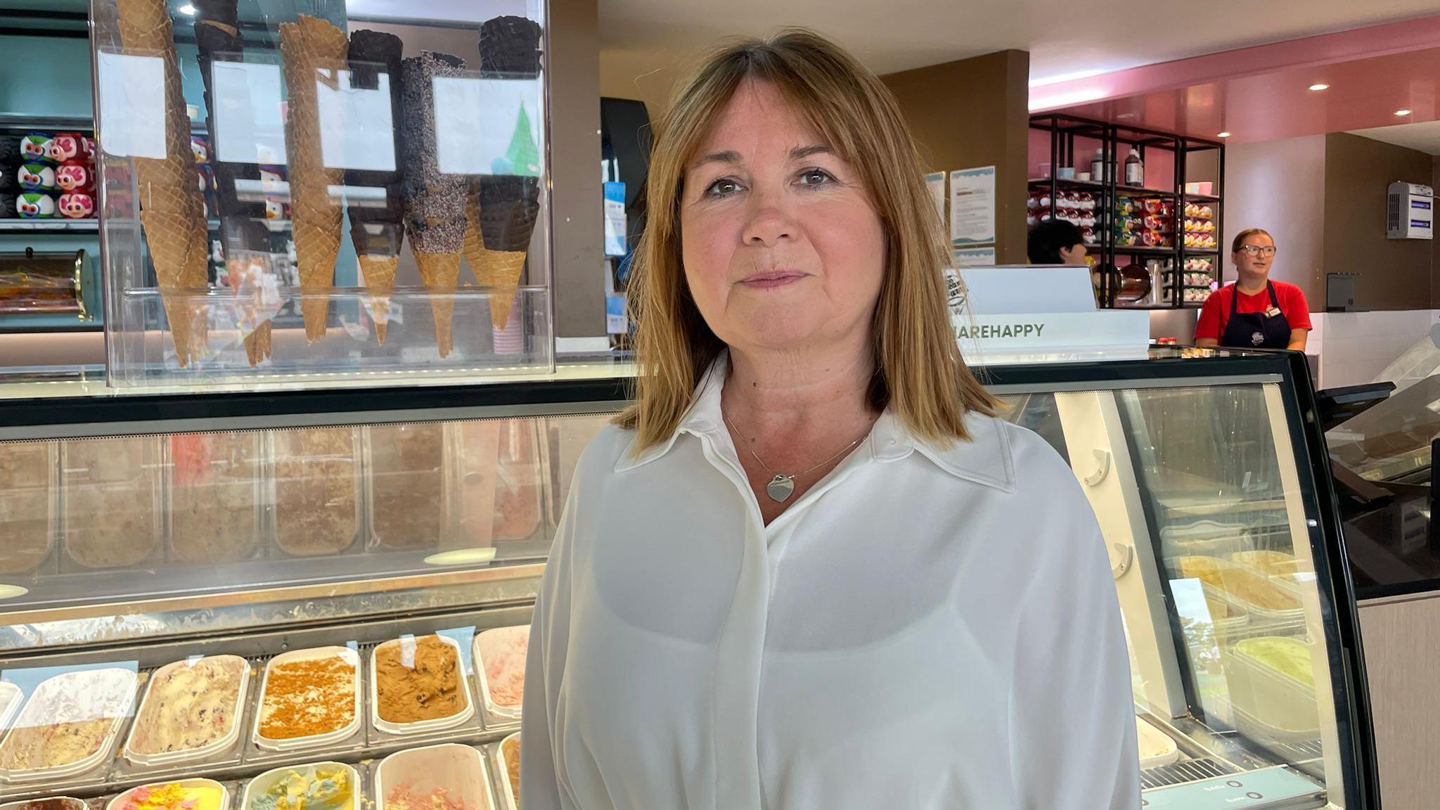 Jane Matthews, a white woman wearing a white blouse, stands in front of an ice cream counter. 