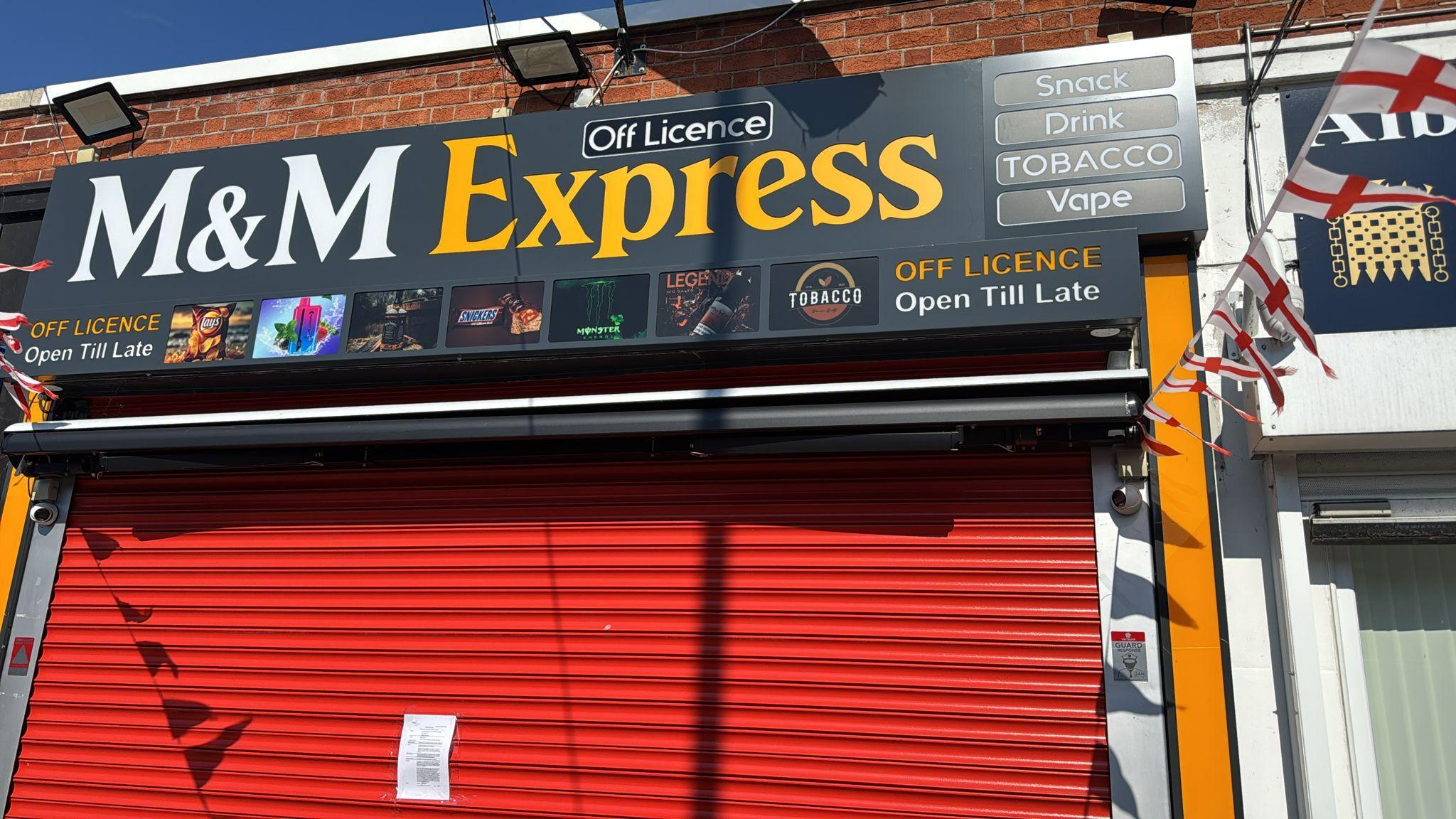 The exterior of a shop with a red shutter and a notice fixed to it.