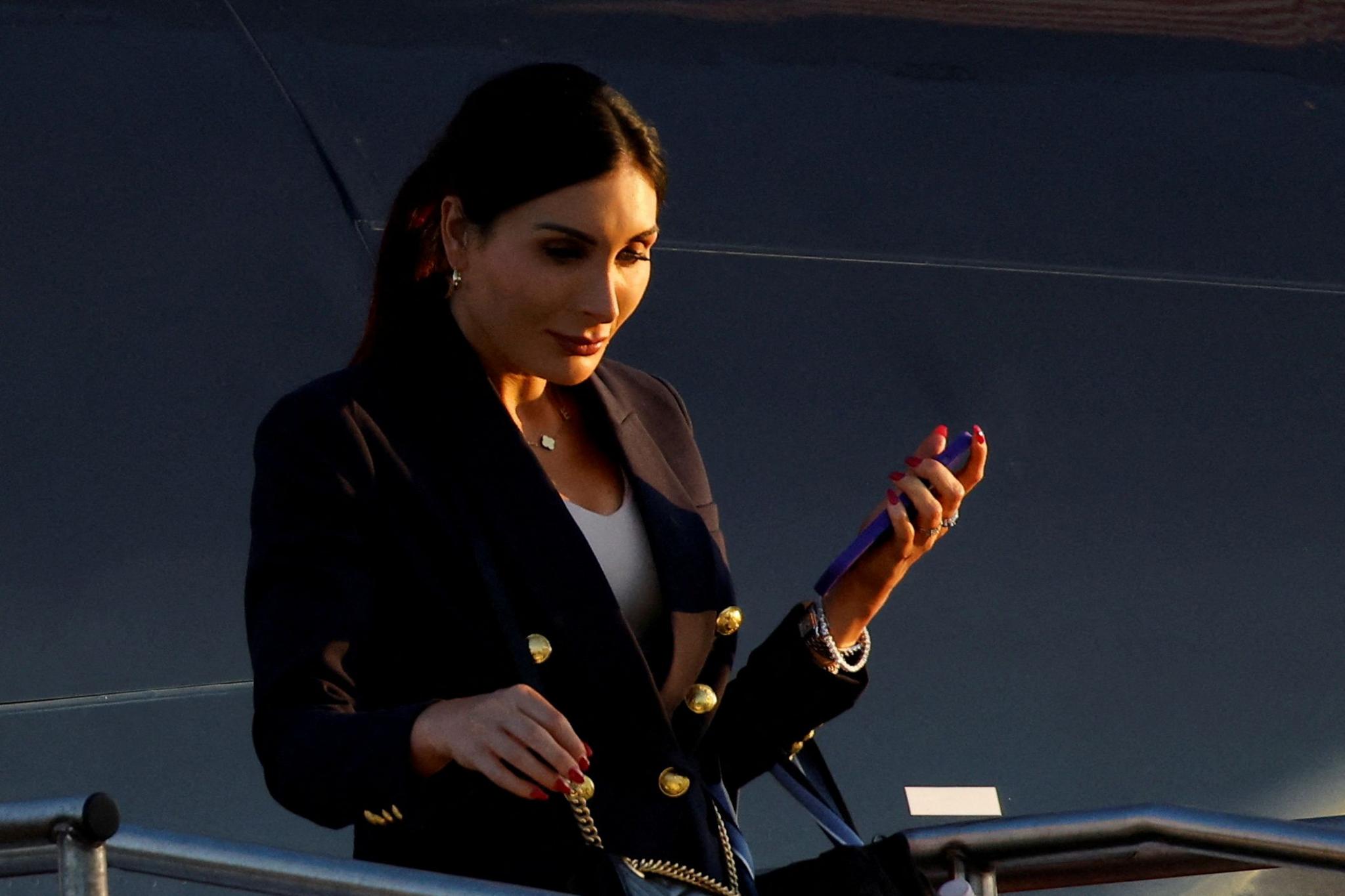 Laura Loomer exiting a plane, looking down and holding a phone in her hand