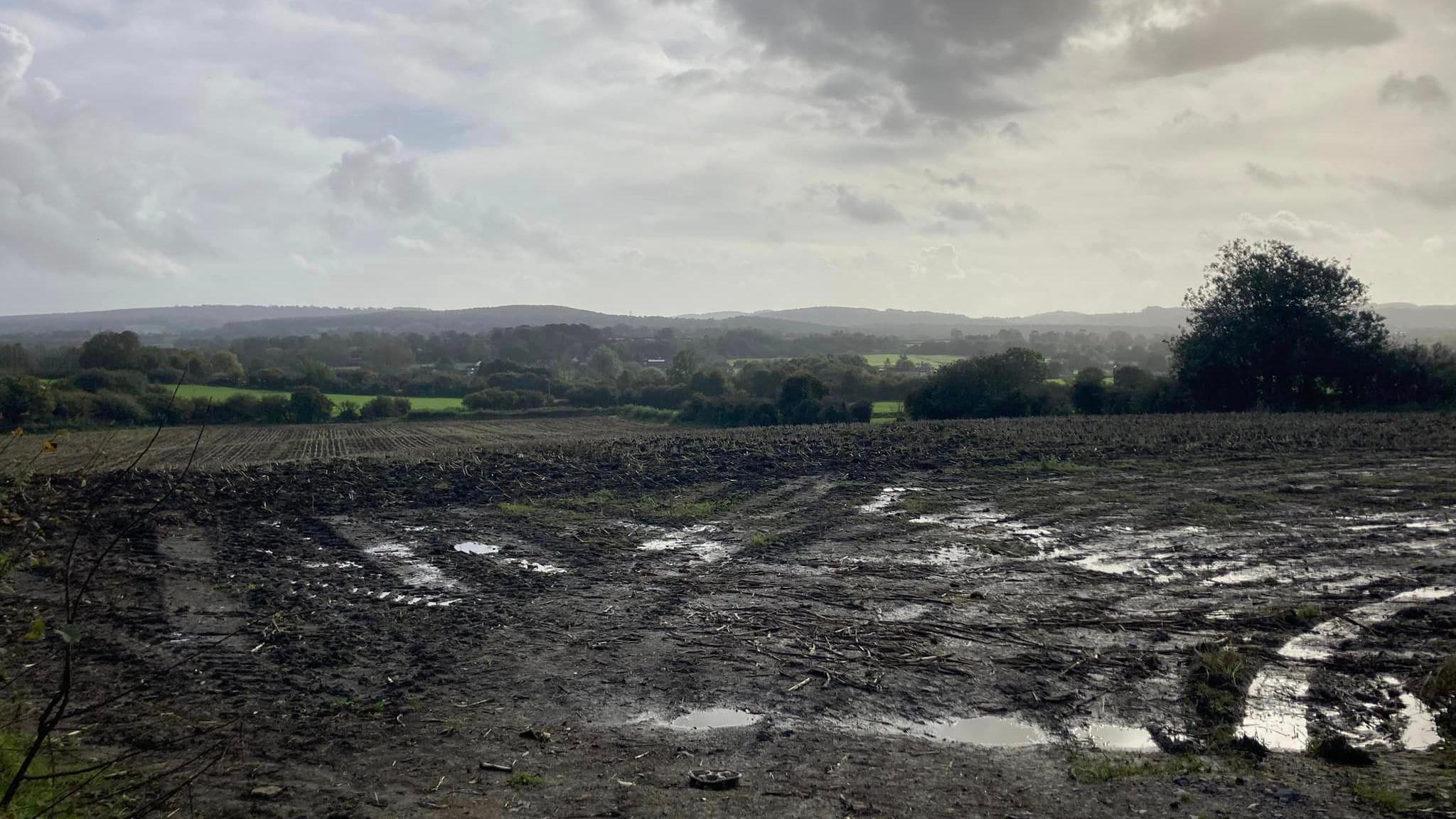 Land between Little Keyford Lane and the A361 in Frome, where the development is planned. It is a field with puddles and mud on it. In the background are hills and trees.