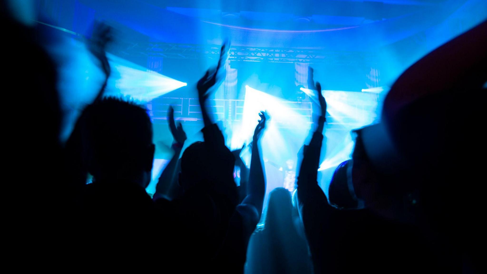 A number of people dancing in silhouette while lights can be seen on stage