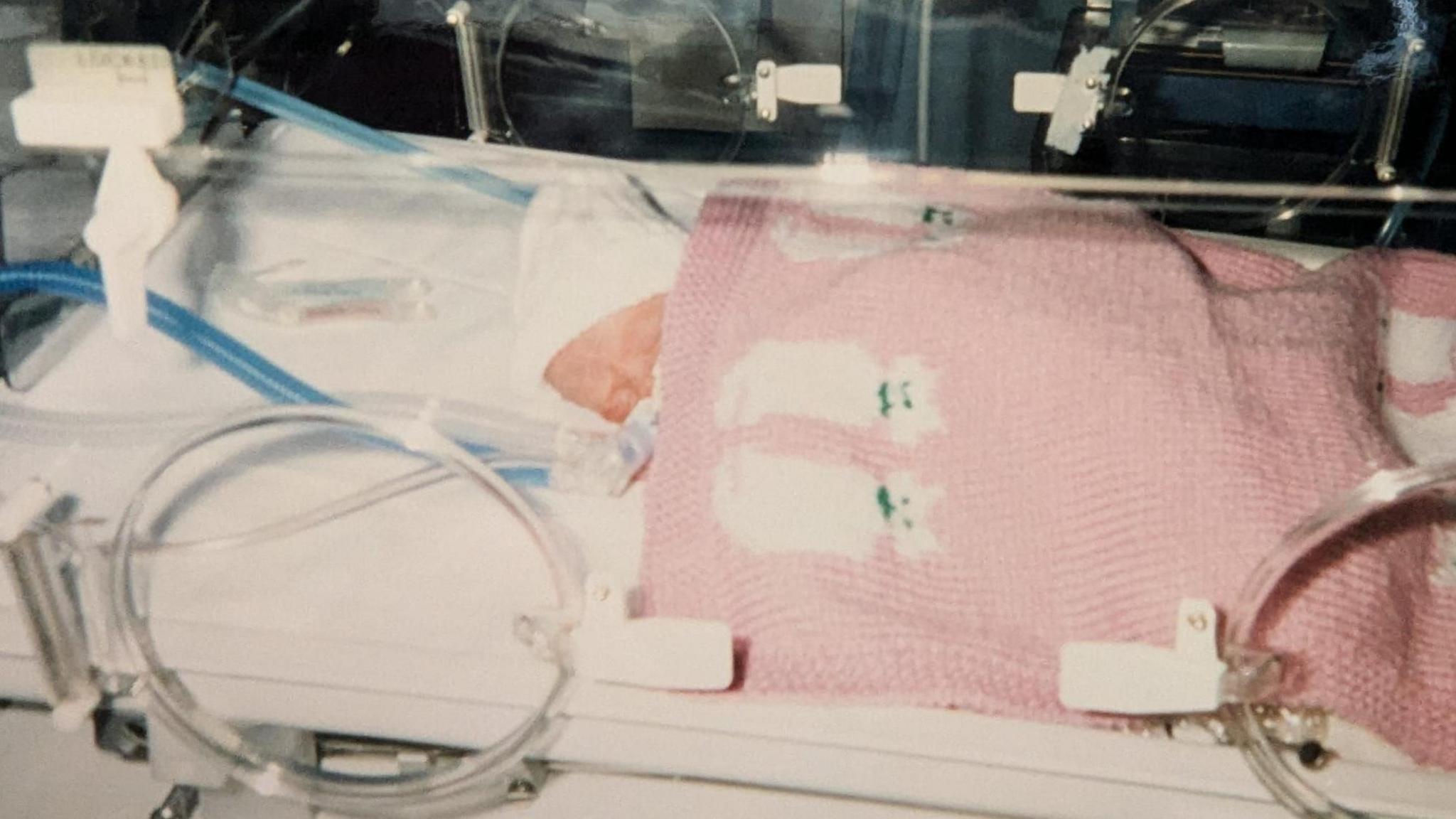 Amy as a baby in an incubator covered by a pink blanket