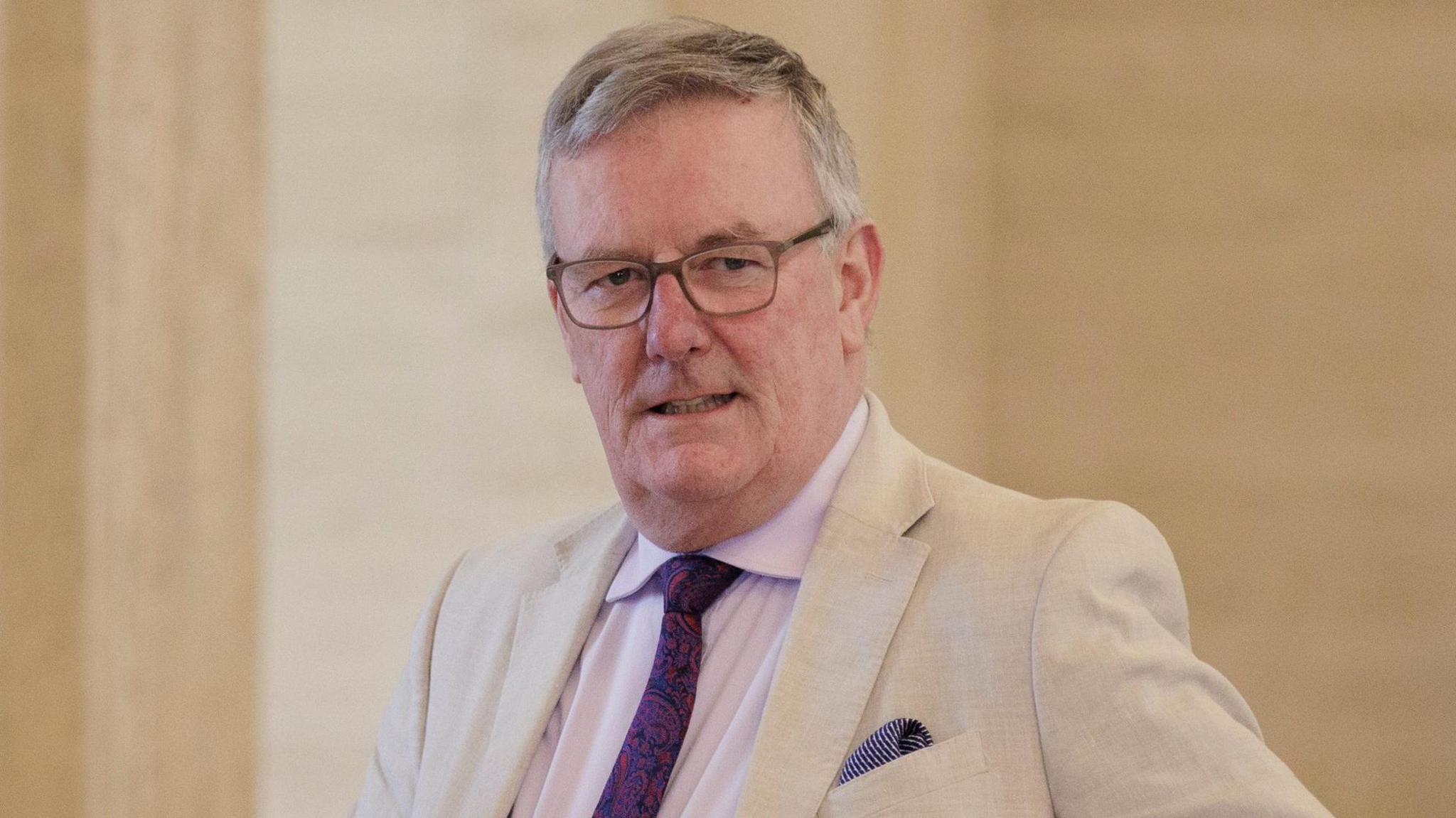 Mike Nesbitt wearing a tan suit and purple tie