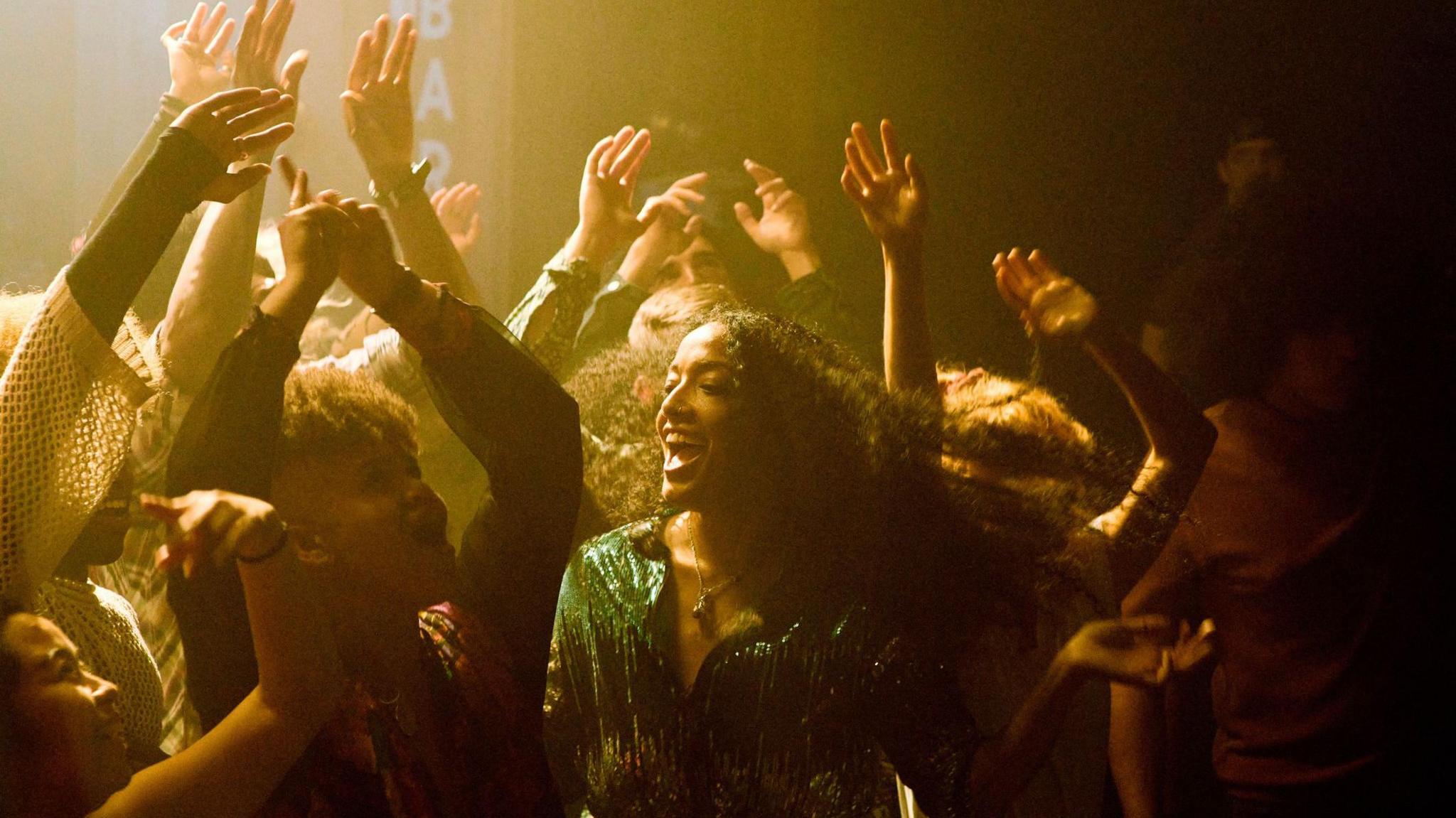 Two girls having fun, dancing in a night club surrounded by people with their hands in the air. 