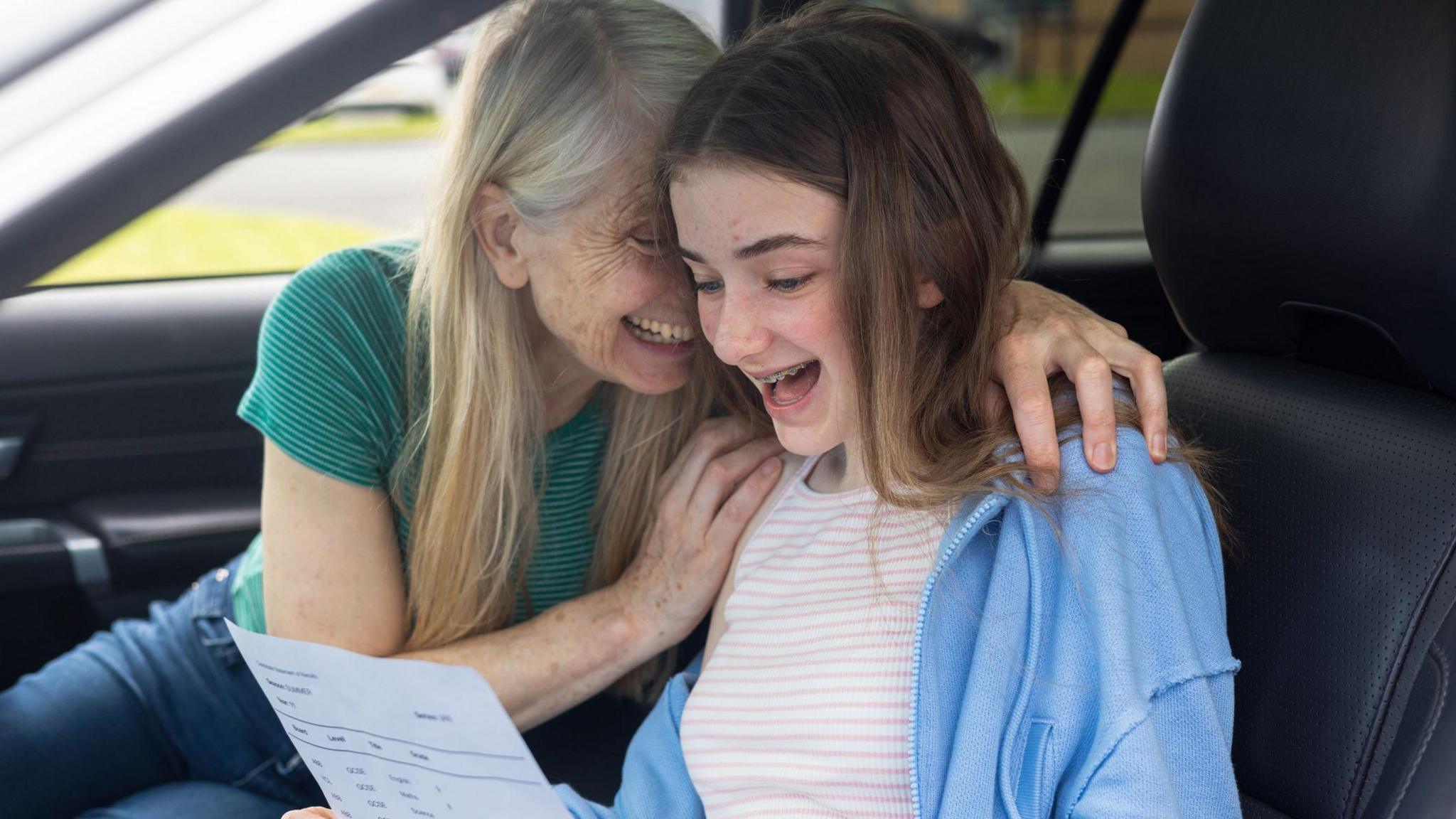 A teenager and their guardian smile in the car after opening exam results