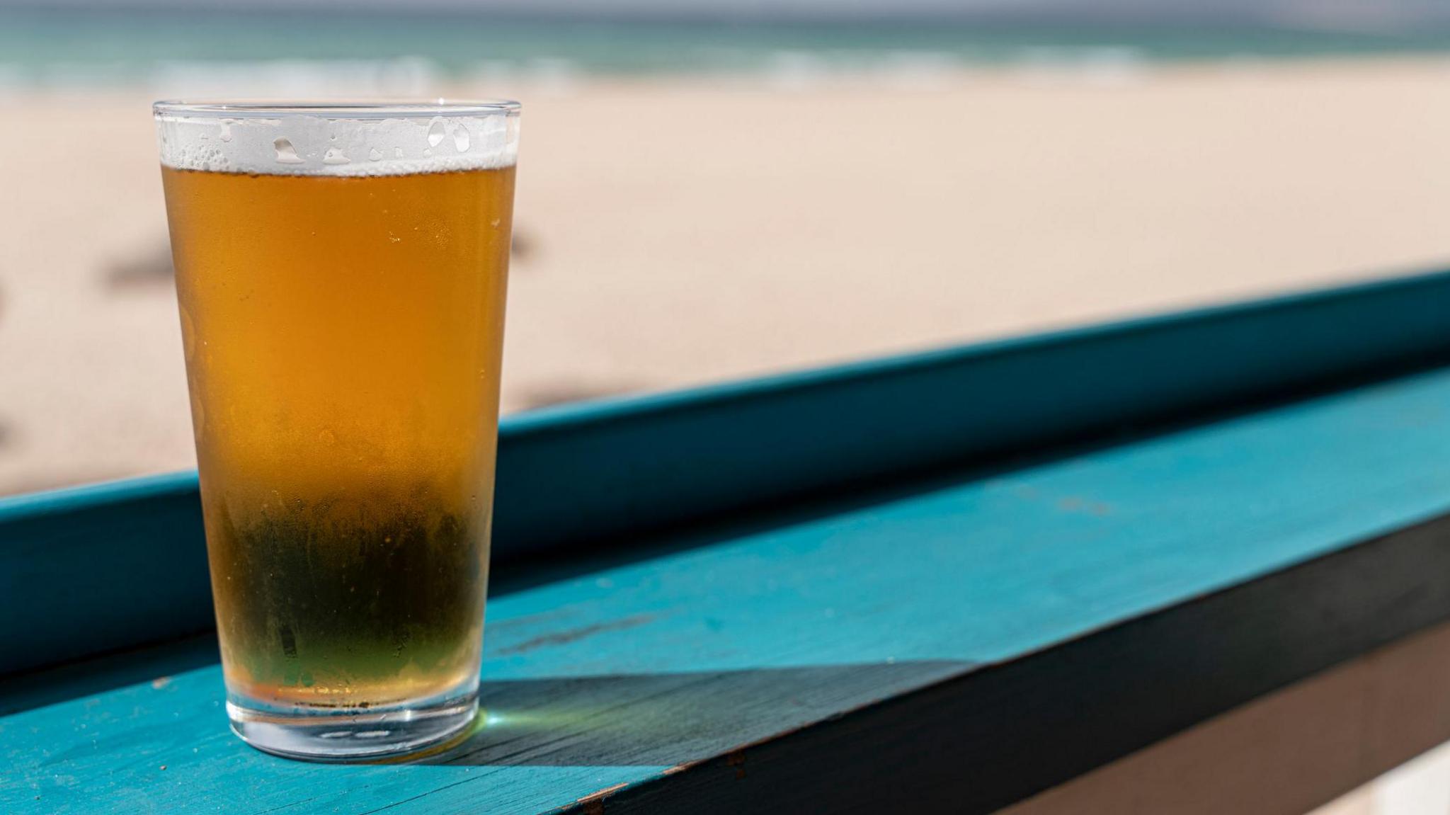 A pint of lager on a turquoise bench.