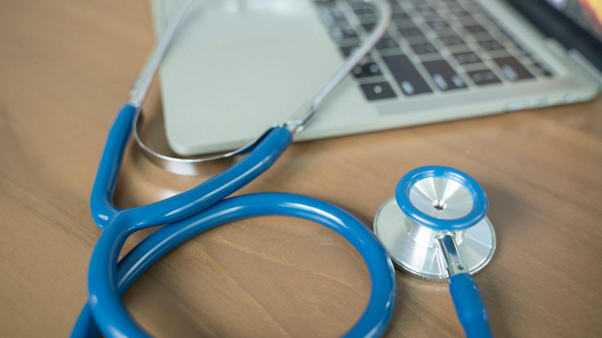 A stethoscope on a table alongside a laptop