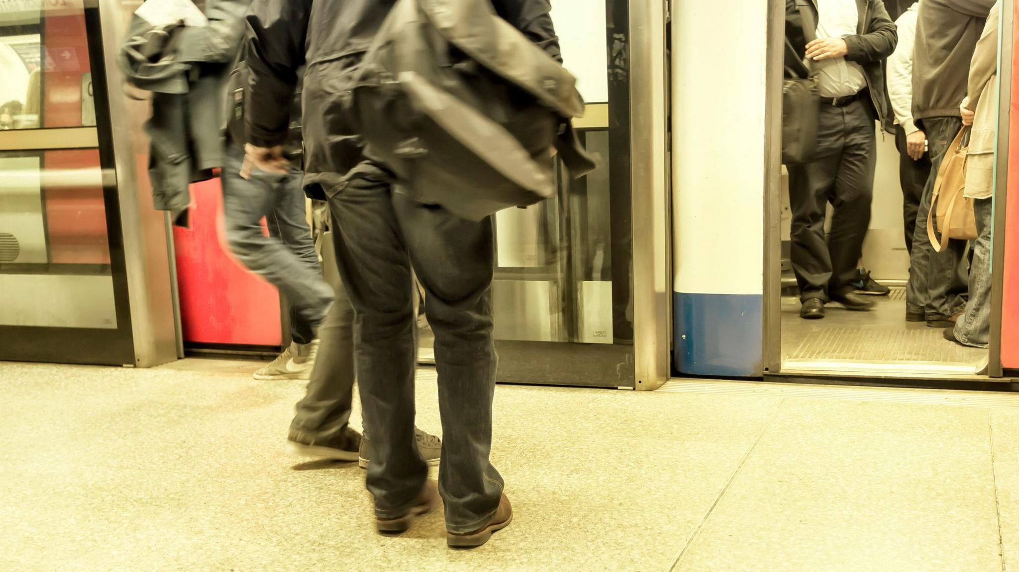People crowd into a London tube carriage, as a person on the platform starts to board. The image only shows the people from below the neck.